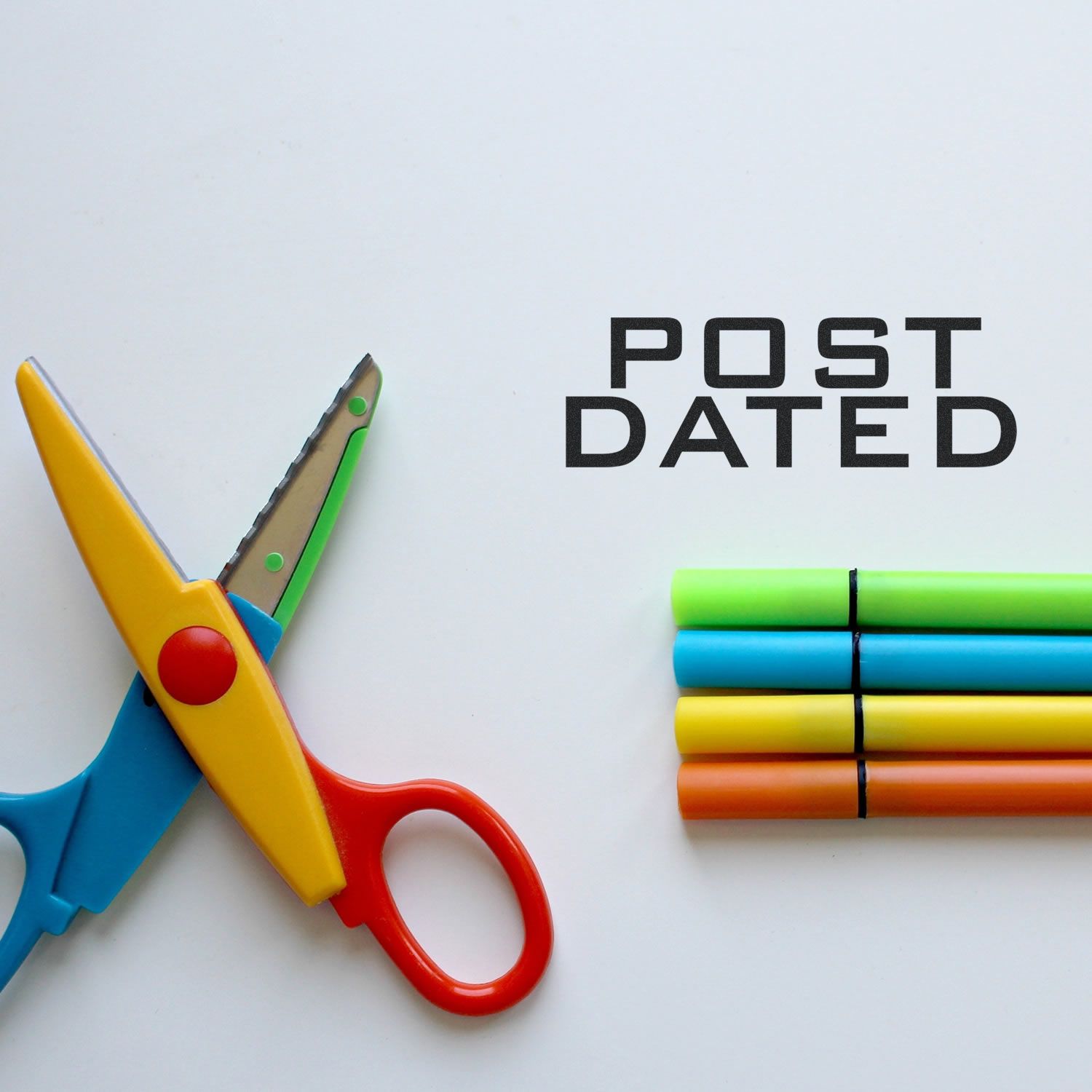 Colorful scissors and markers next to a Post Dated rubber stamp impression on a white surface.