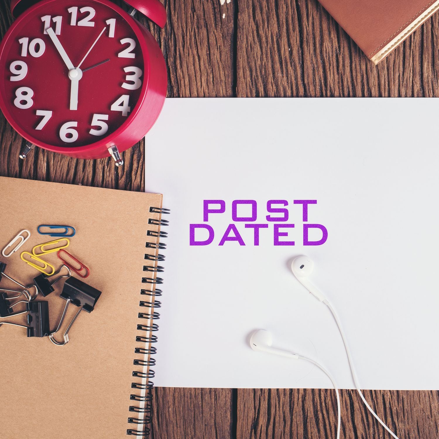 Large Self Inking Post Dated Stamp in purple ink on white paper, surrounded by a red clock, notebooks, paper clips, and earphones.