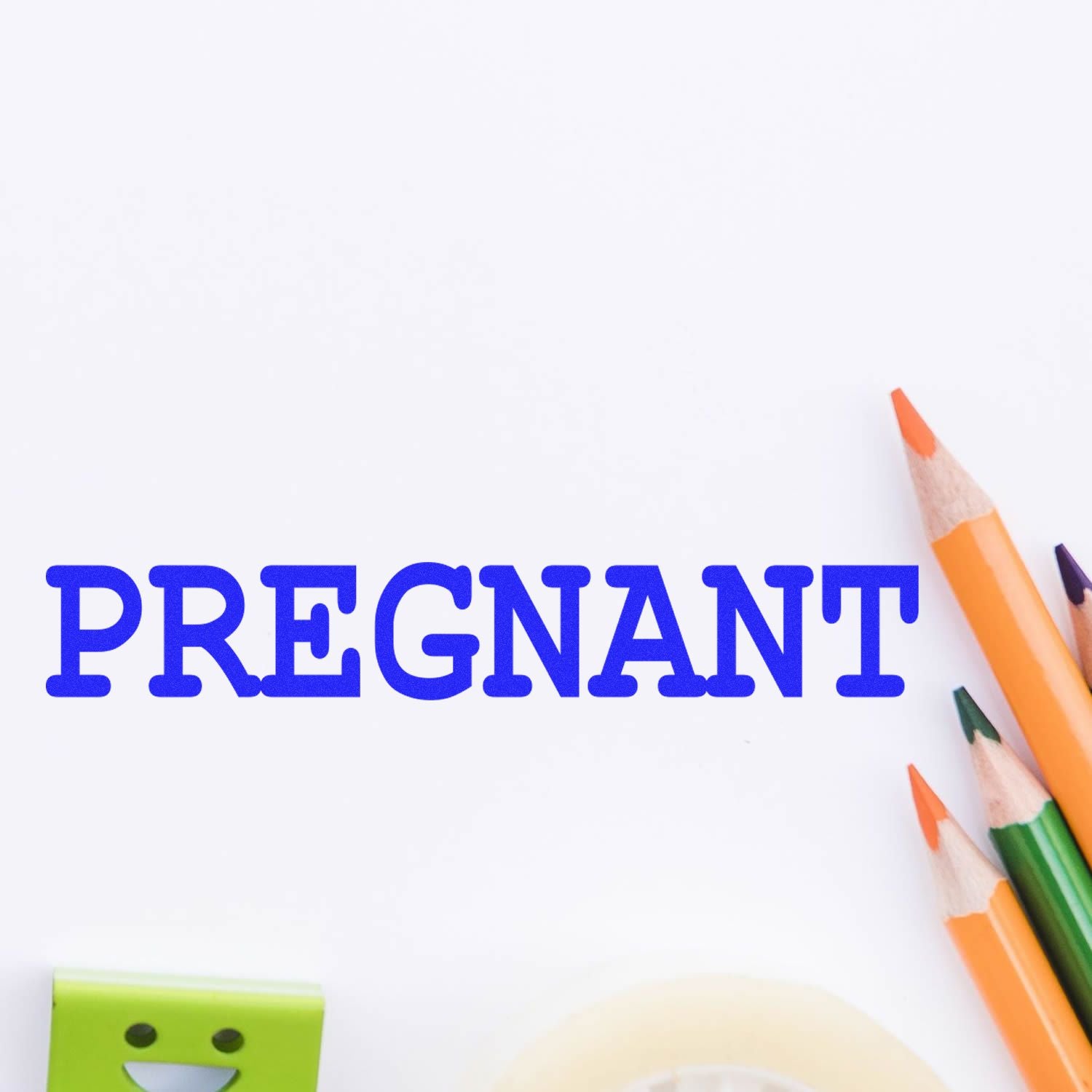 Pregnant rubber stamp in blue ink on white paper, surrounded by colorful pencils and stationery items.