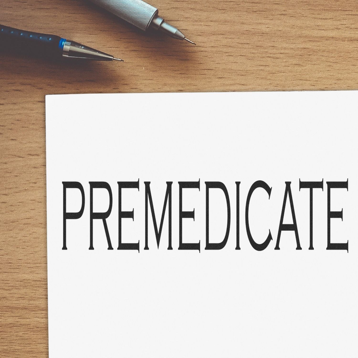 Premedicate rubber stamp impression on white paper with a pen in the background on a wooden surface.