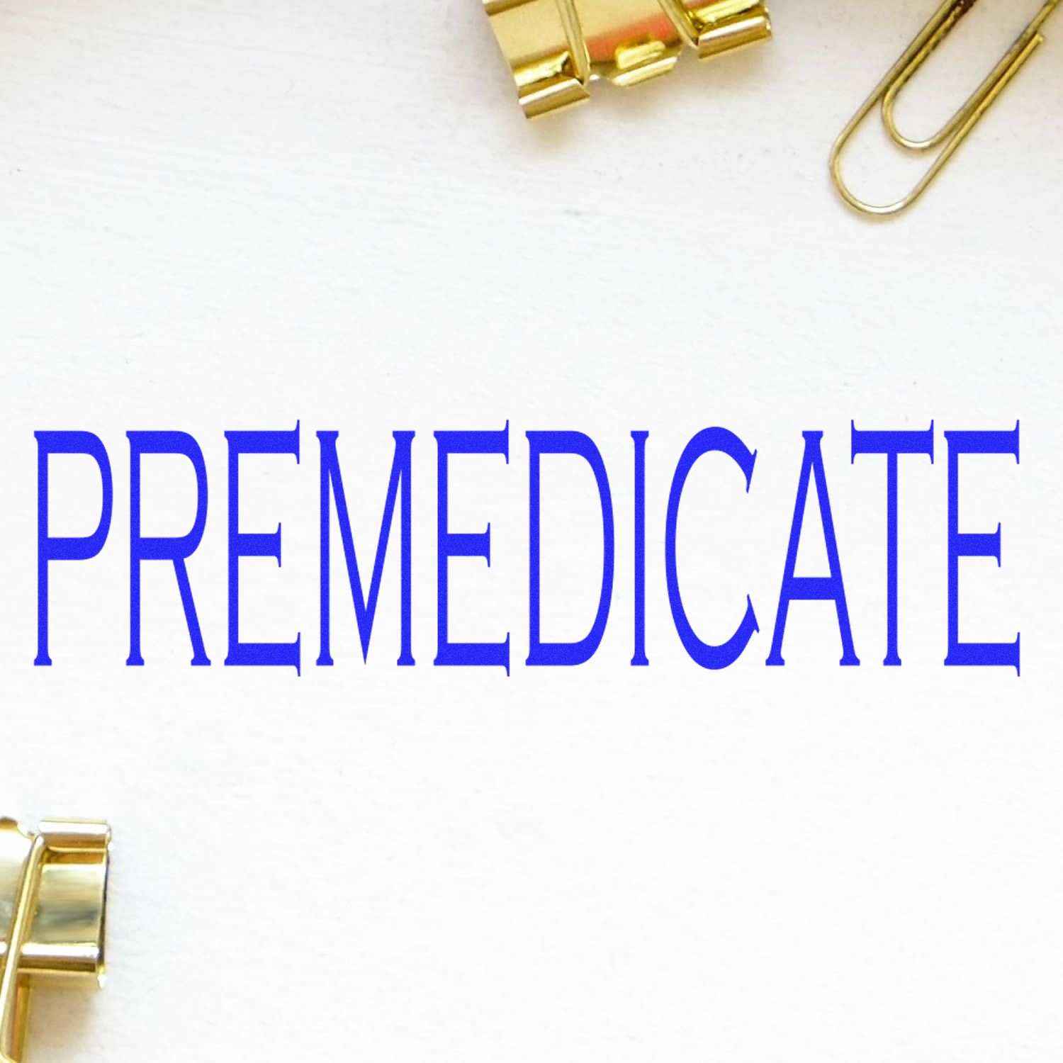 Self Inking Premedicate Stamp in use, displaying the word PREMEDICATE in blue ink on a white surface with gold paper clips nearby.