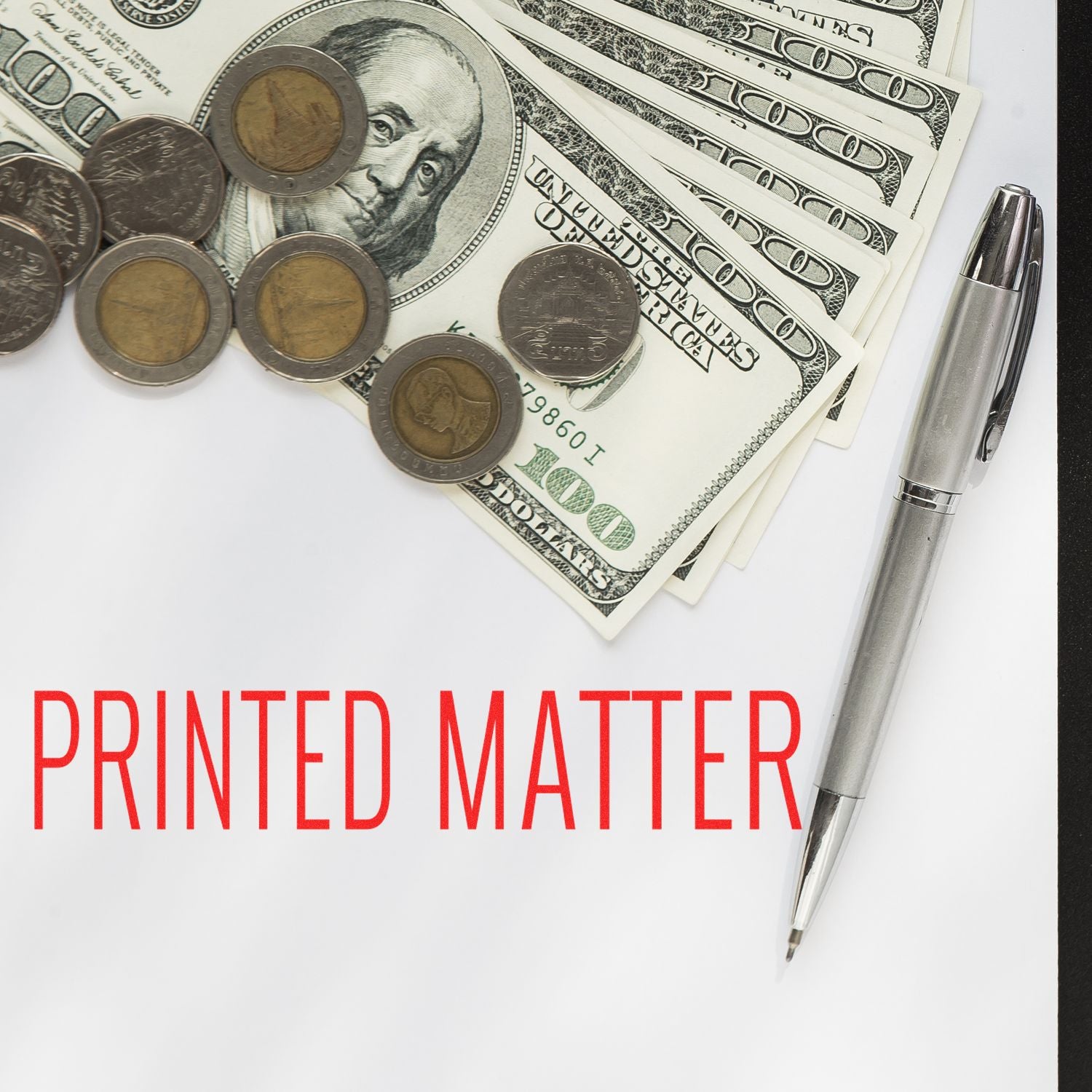 Slim Pre-Inked Printed Matter Stamp on white paper with red text, surrounded by dollar bills, coins, and a silver pen.