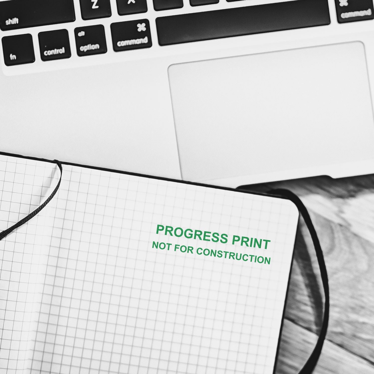 Slim Pre-Inked Progress Print Stamp in green ink on a notebook with a laptop in the background.