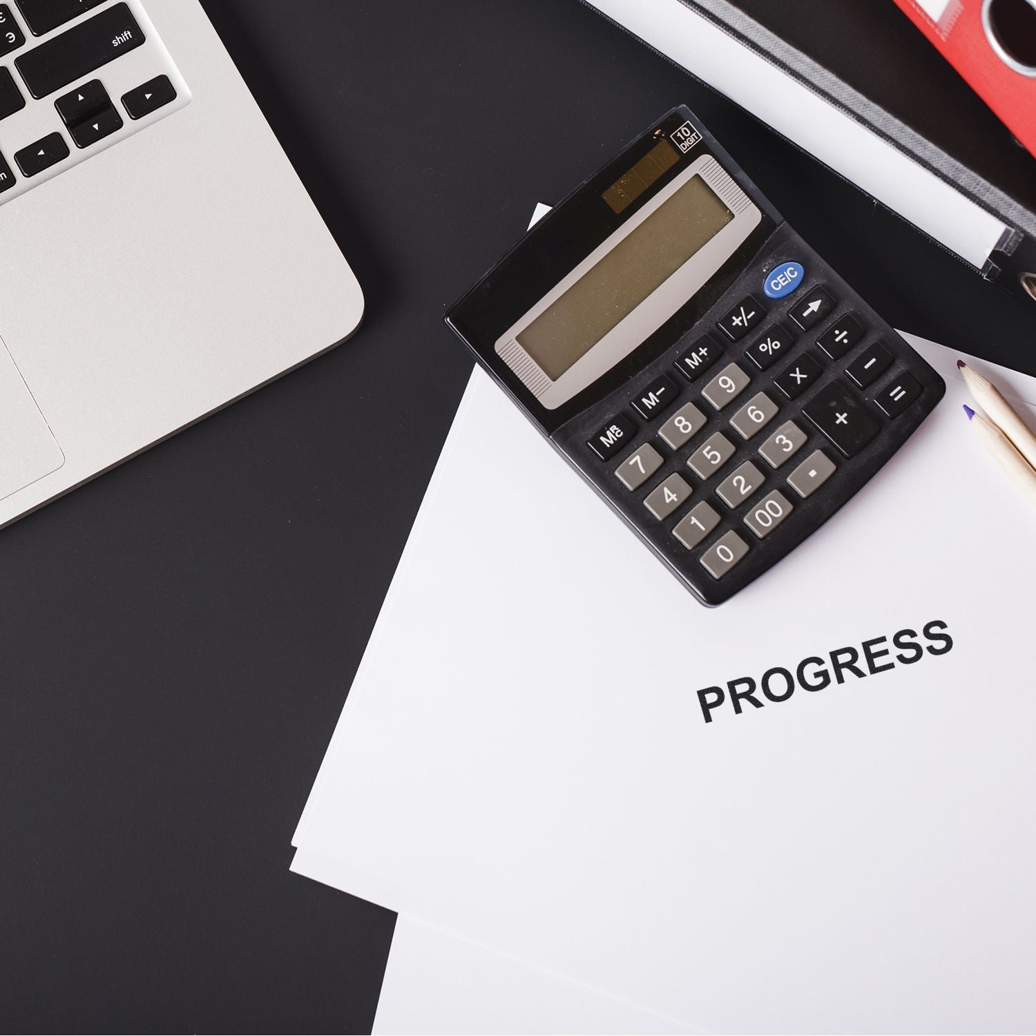 A Self Inking Progress Stamp is placed on a desk with a calculator, a pencil, and a stack of papers labeled PROGRESS next to a laptop.