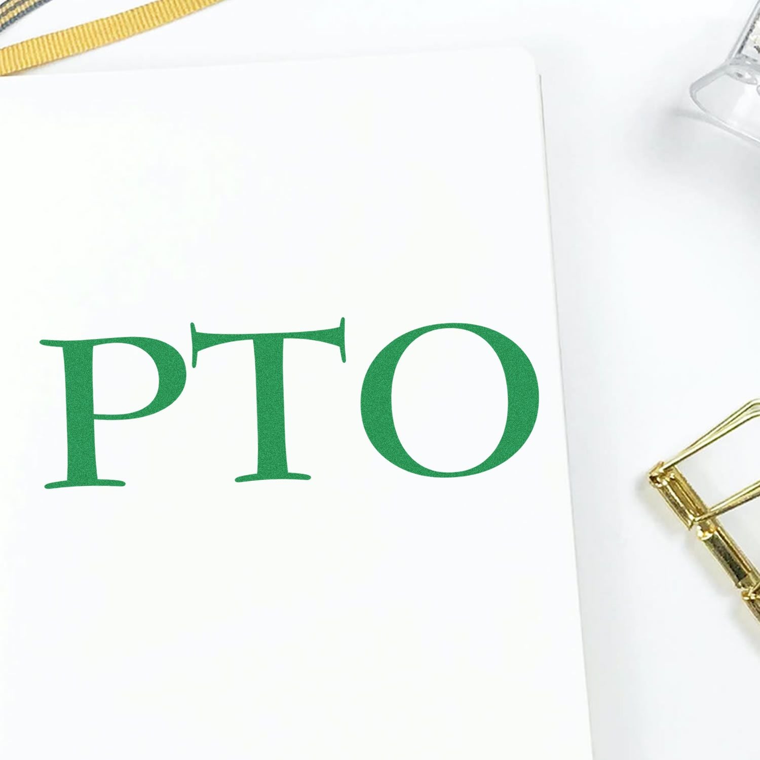 Large Self Inking PTO Stamp imprinting PTO in green on white paper, with a gold pen and clear stamp holder nearby.