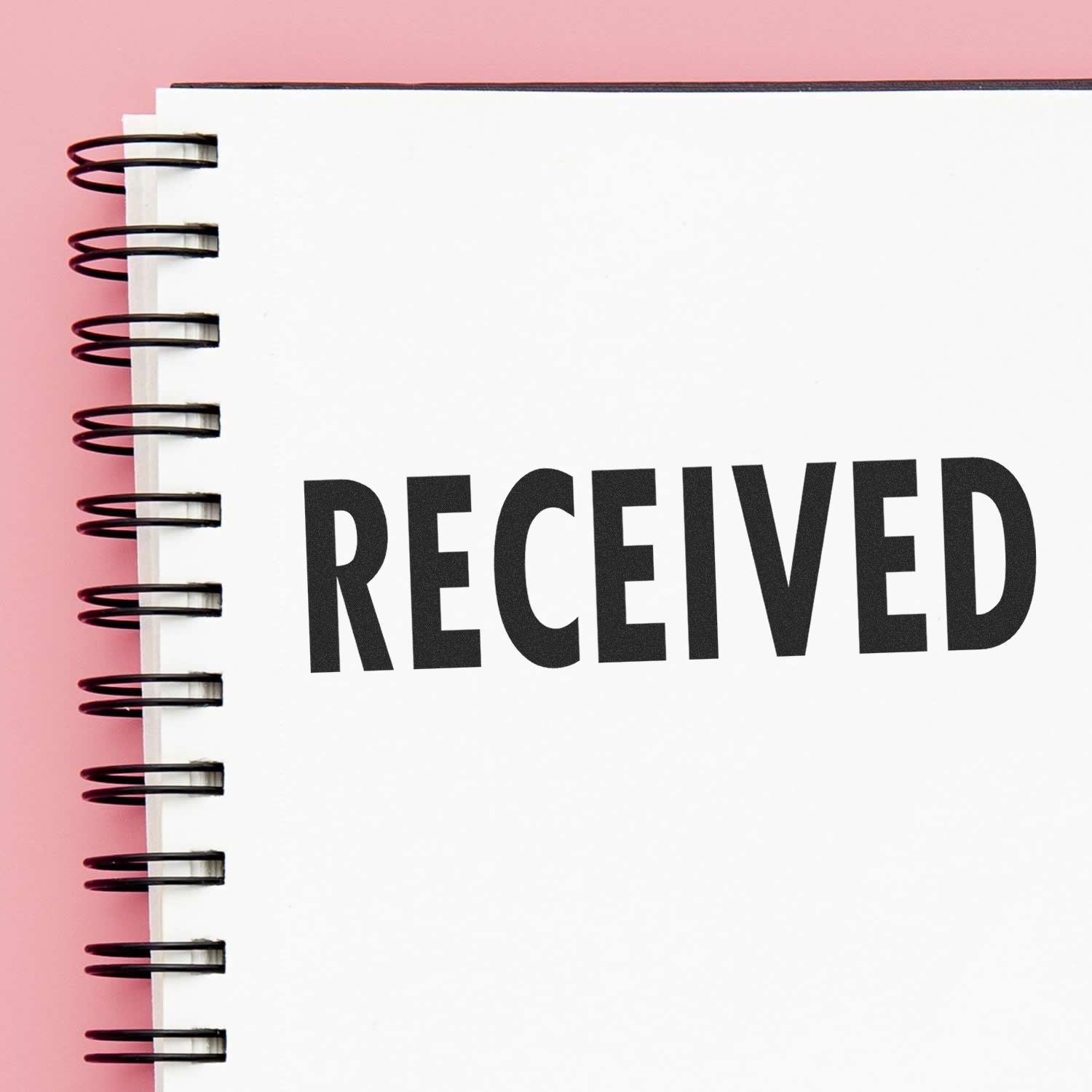 Self Inking Received Stamp marking RECEIVED in bold black letters on a spiral-bound notebook with a pink background.