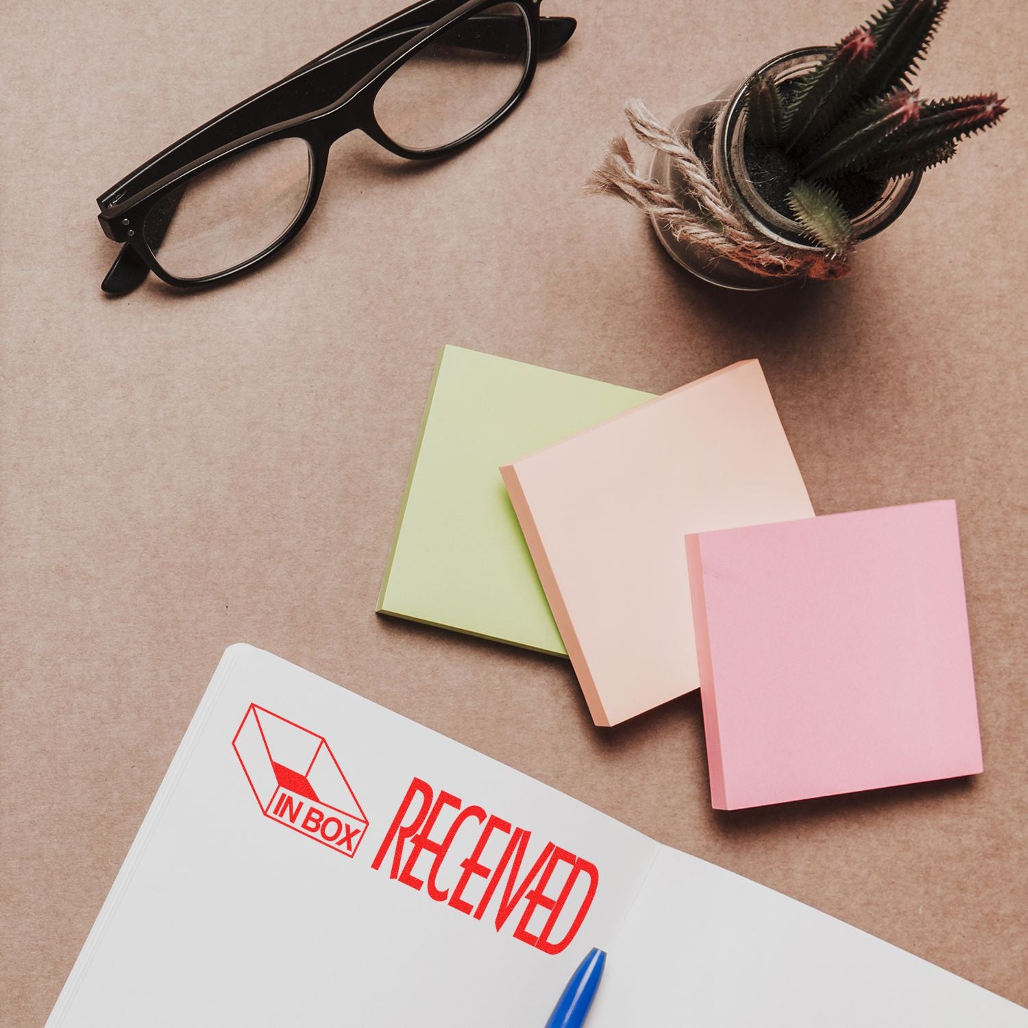 Large Self Inking Received with In Box Icon Stamp marking a document, surrounded by sticky notes, glasses, and a small plant.