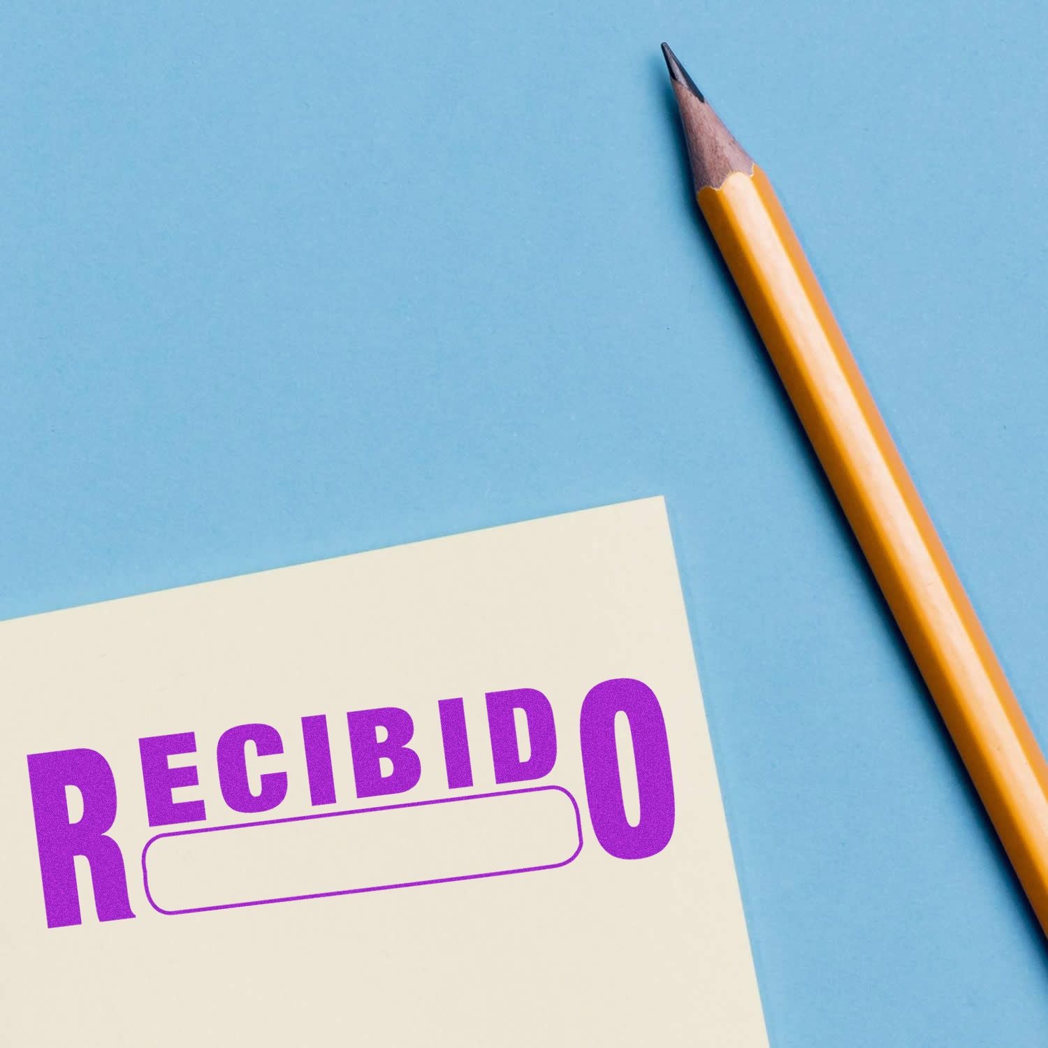 Slim Pre-Inked Recibido Stamp in purple ink on a paper next to a yellow pencil on a blue background.