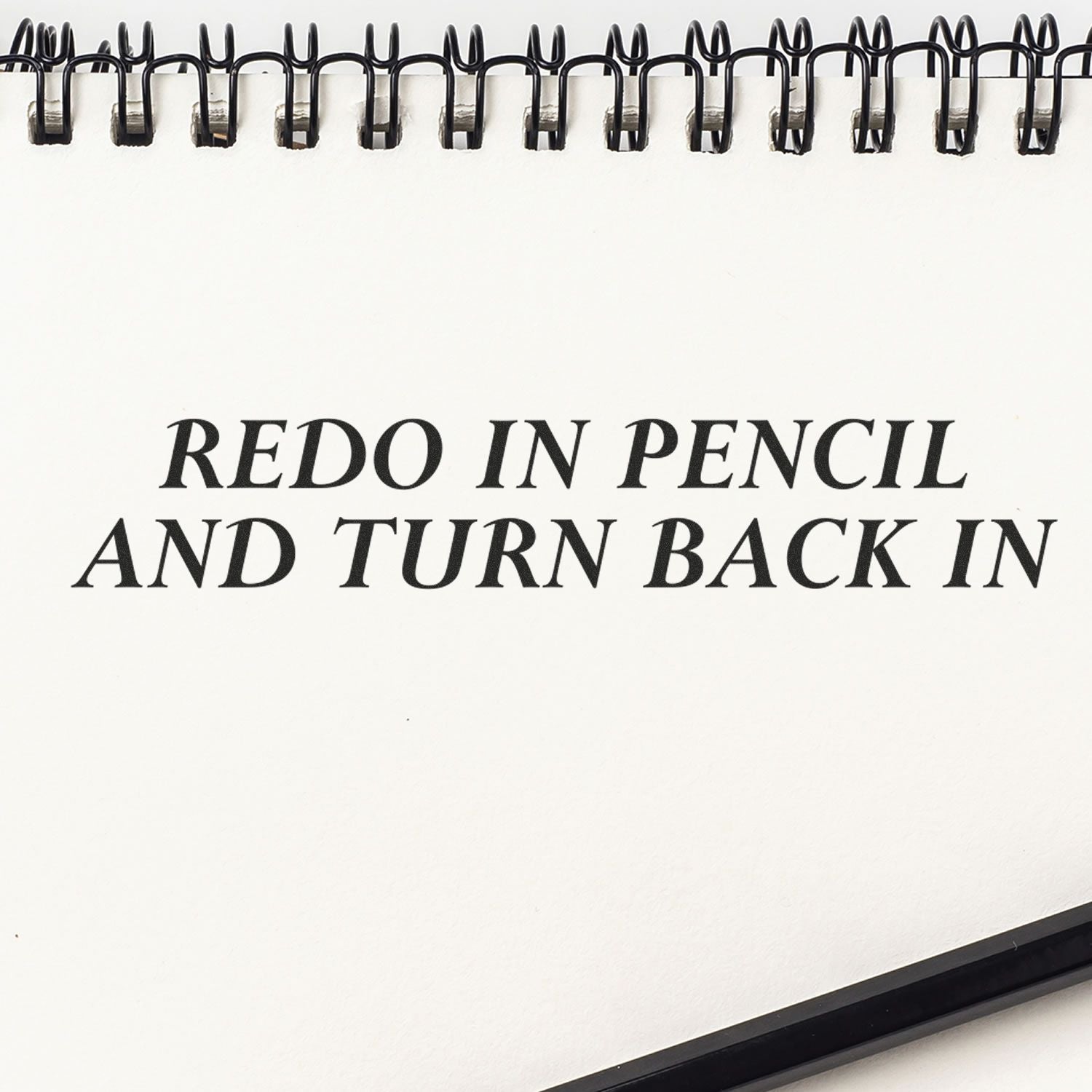 Self Inking Redo In Pencil And Turn Back In Stamp imprint on a spiral notebook page with a pencil at the bottom right corner.