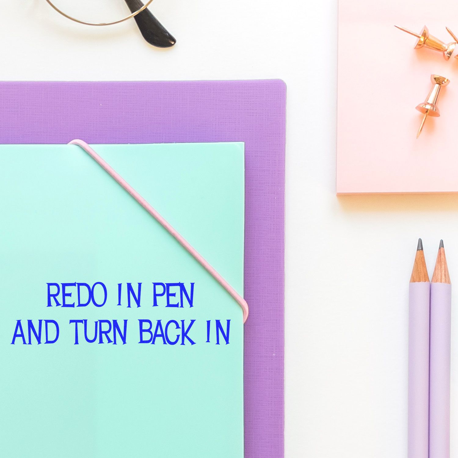 Large Self Inking Redo In Pen And Turn Back In Stamp on a mint green folder, surrounded by pencils, push pins, and a purple notebook.