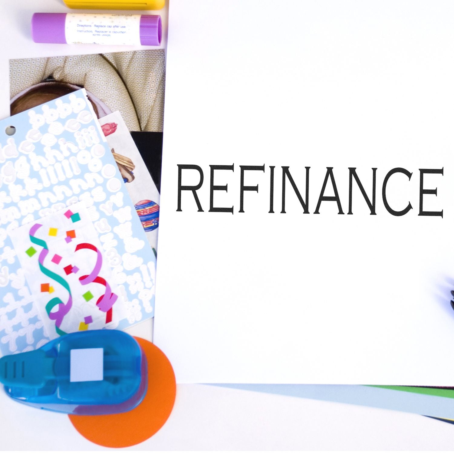 Refinance rubber stamp on white paper surrounded by colorful office supplies including markers, stickers, and a stapler.