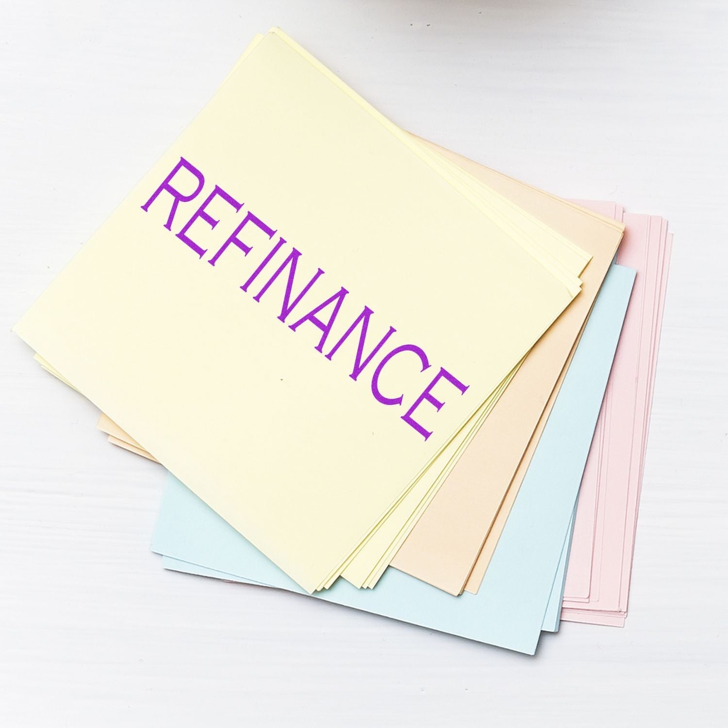 Stack of pastel-colored papers stamped with REFINANCE using the Self Inking Refinance Stamp, placed on a white surface.