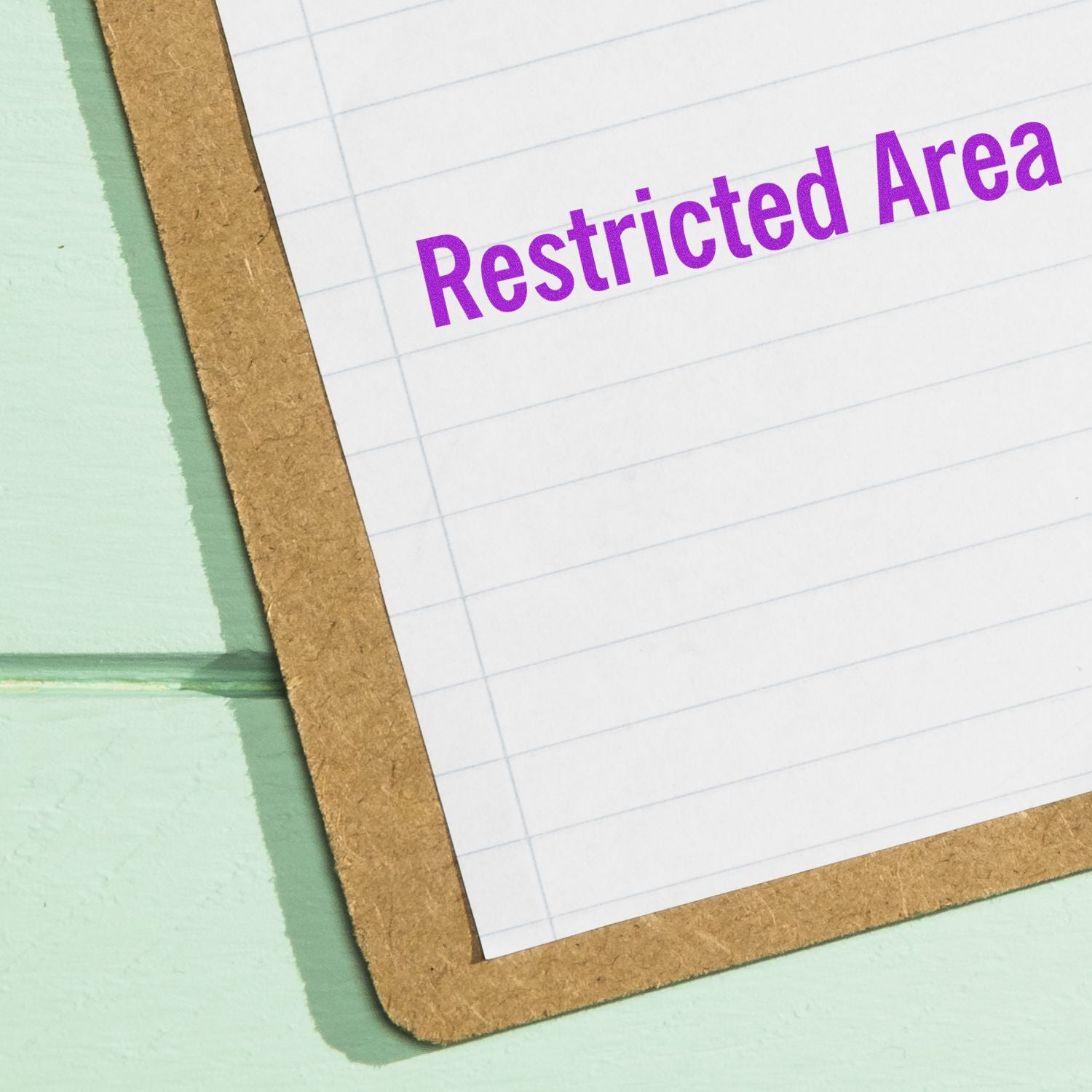 A piece of paper stamped with Restricted Area in purple ink using the Large Pre-Inked Restricted Area Stamp, placed on a green surface.