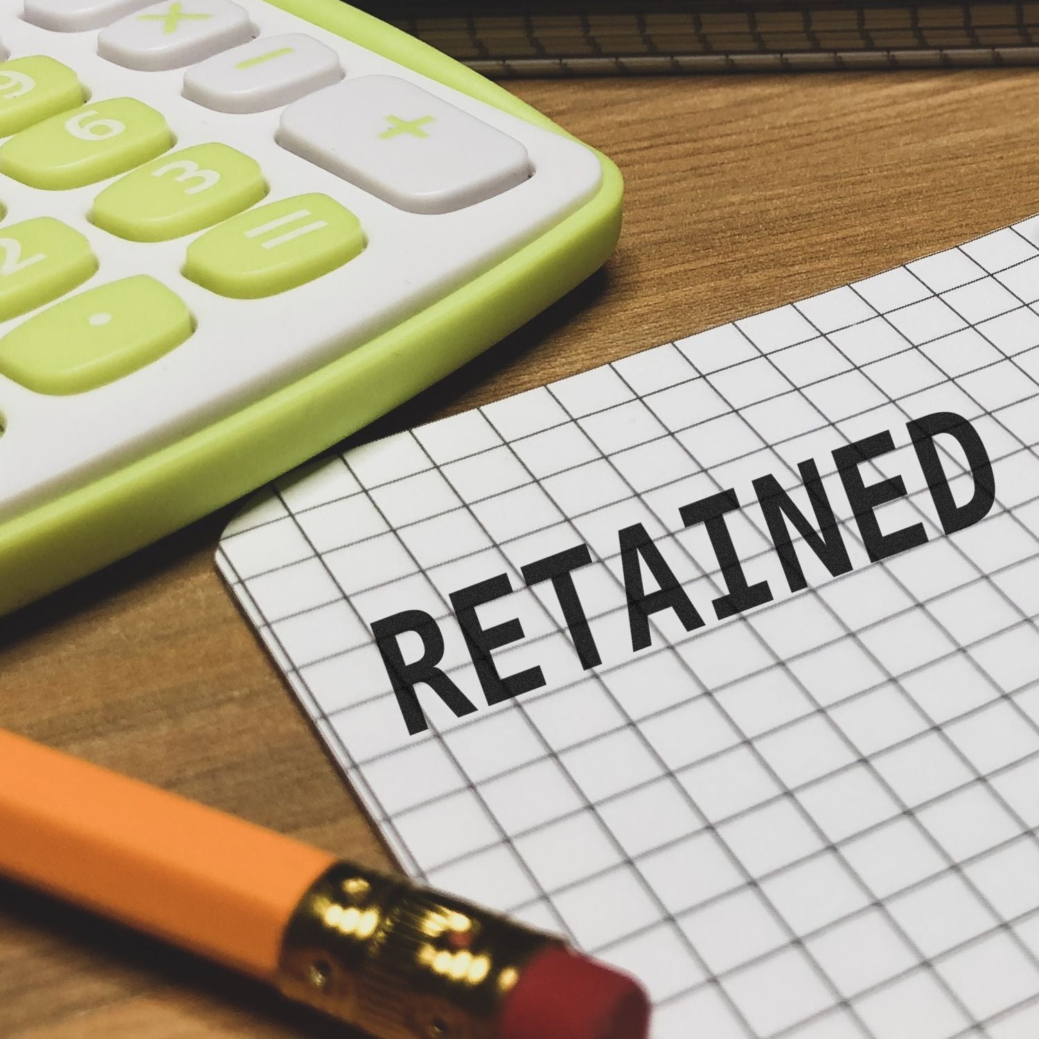 Retained rubber stamp on graph paper next to a pencil and calculator on a wooden desk.