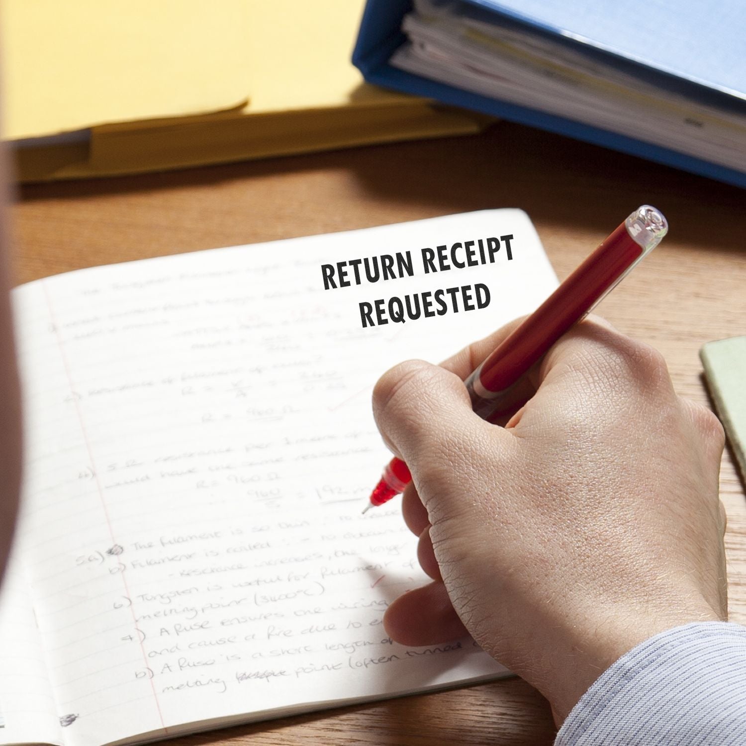 Hand holding a red pen writing in a notebook with the Self Inking Return Receipt Requested Stamp marking the page.