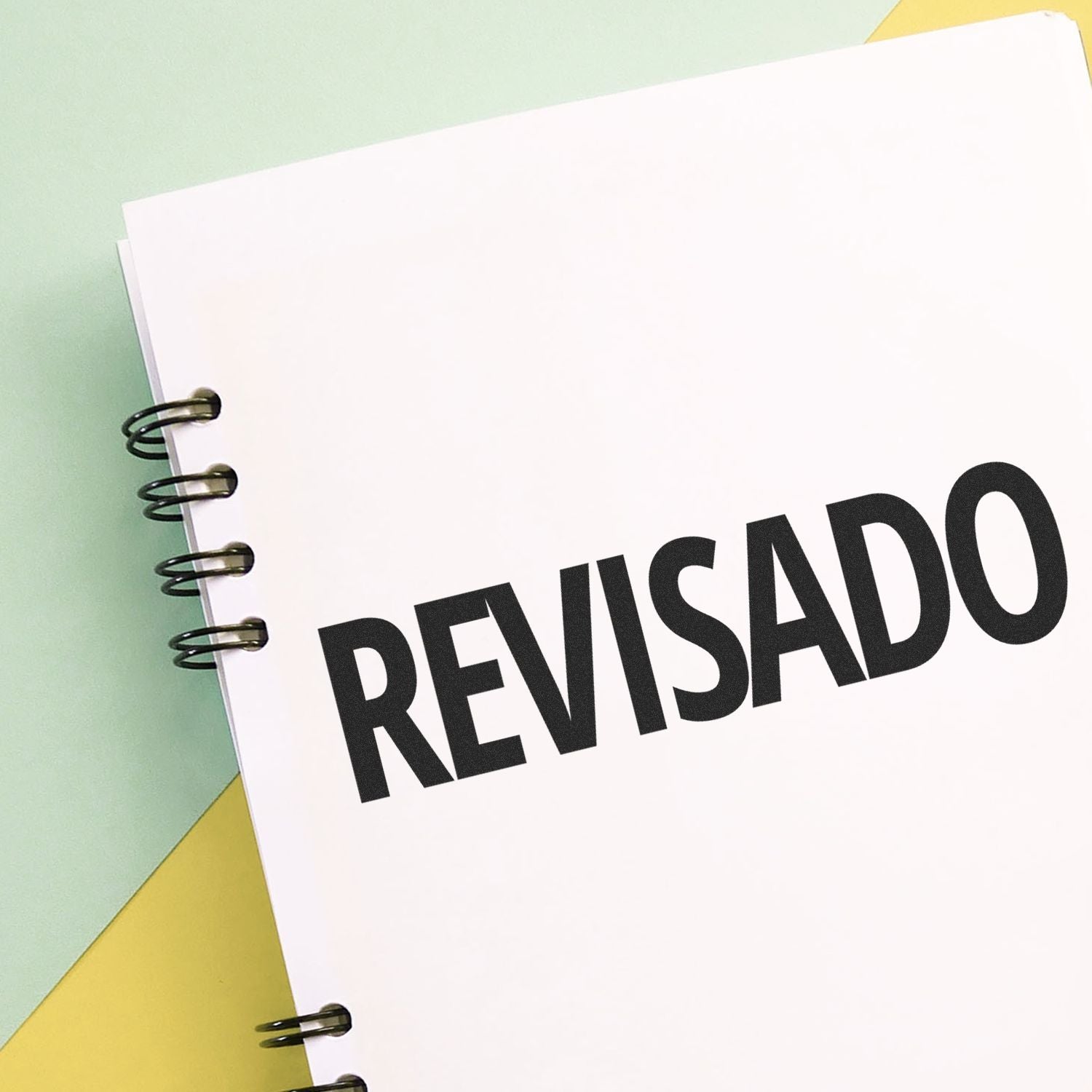 A notebook with REVISADO stamped on a page using the Large Self Inking Revisado Stamp, placed on a pastel-colored background.