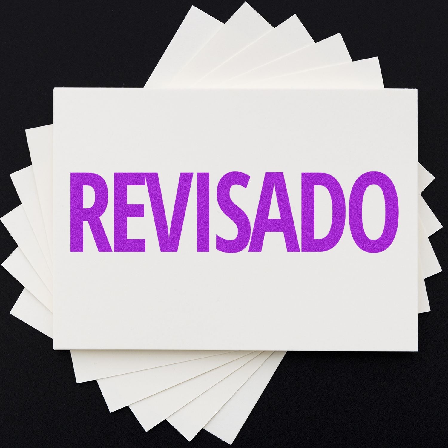 A stack of white cards with the top card stamped in purple ink with the word 'REVISADO' using a Revisado Rubber Stamp.