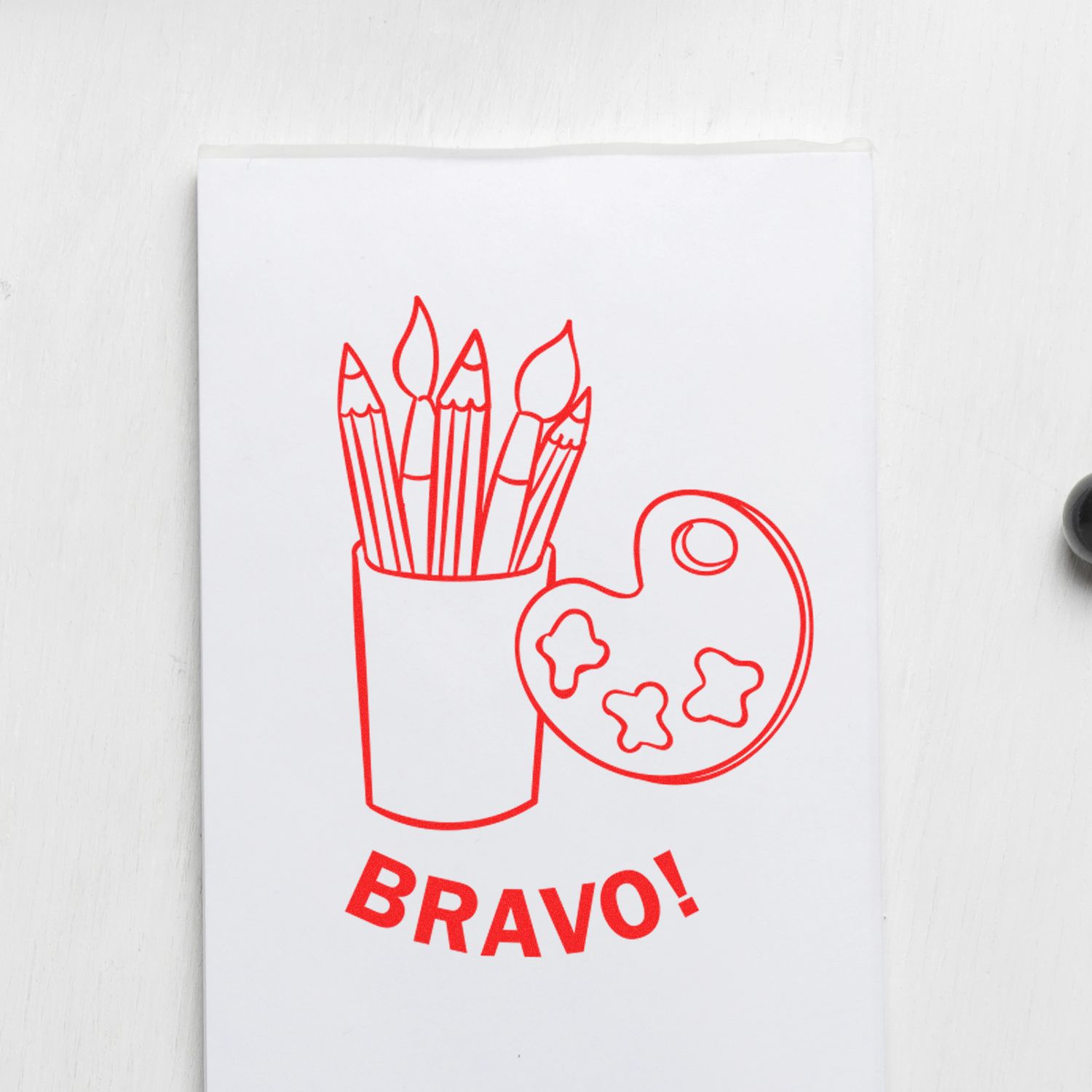 Round Bravo Rubber Stamp featuring a design of paintbrushes in a cup and a palette with the word 'BRAVO!' below.