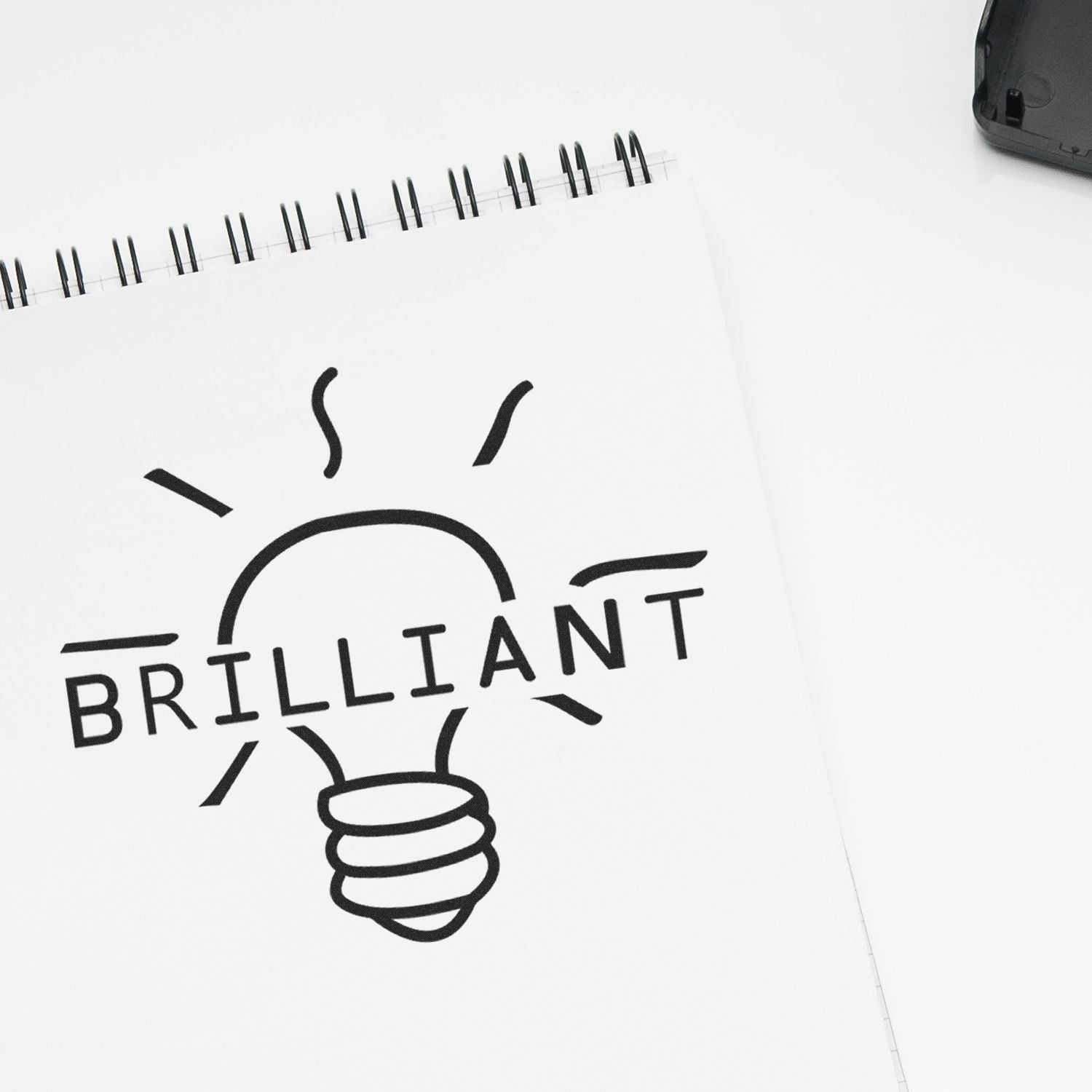 Round Brilliant Rubber Stamp imprint on a notebook, featuring a light bulb design with the word 'BRILLIANT' inside.