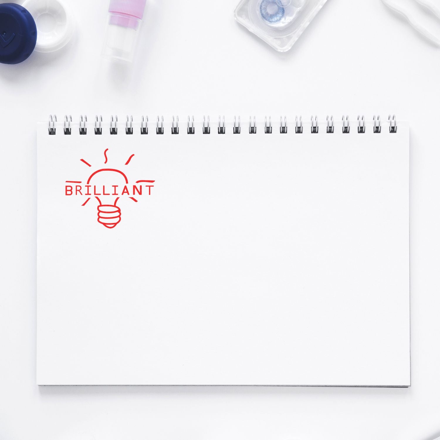 Round Brilliant Rubber Stamp imprint on a spiral notebook with a light bulb design and the word 'BRILLIANT' in red ink.