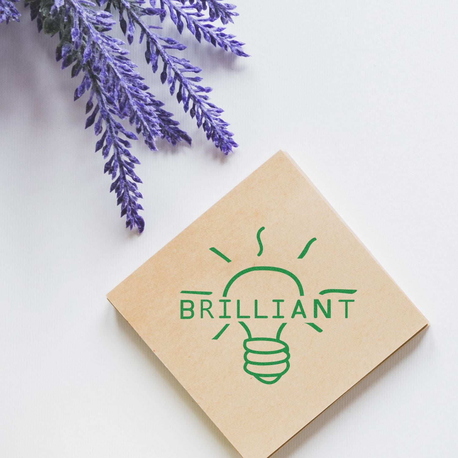 Round Brilliant Rubber Stamp on a brown square card with a green lightbulb design and the word BRILLIANT, next to lavender sprigs.