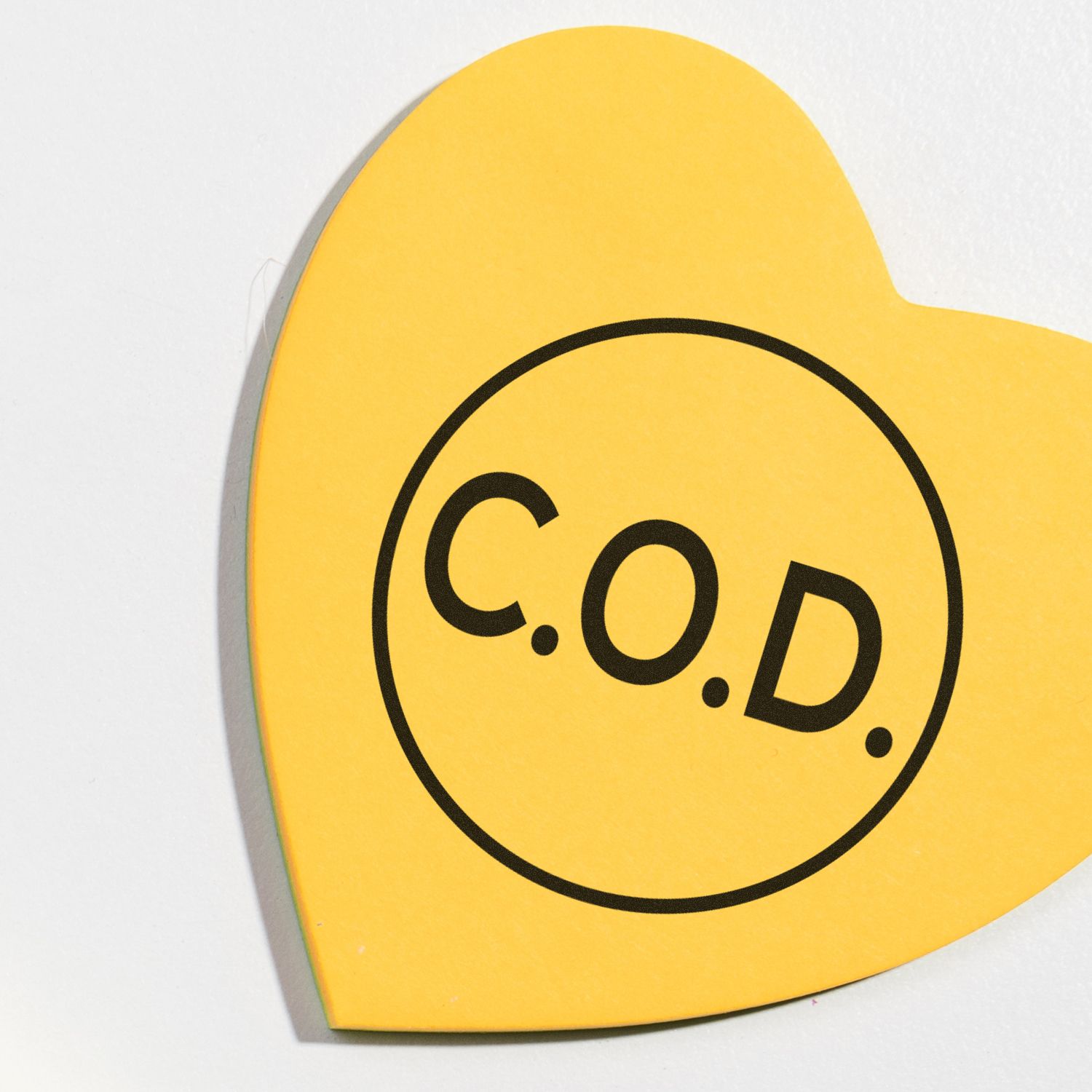 Yellow heart-shaped paper with a round COD rubber stamp imprint in the center, featuring bold black letters C.O.D.