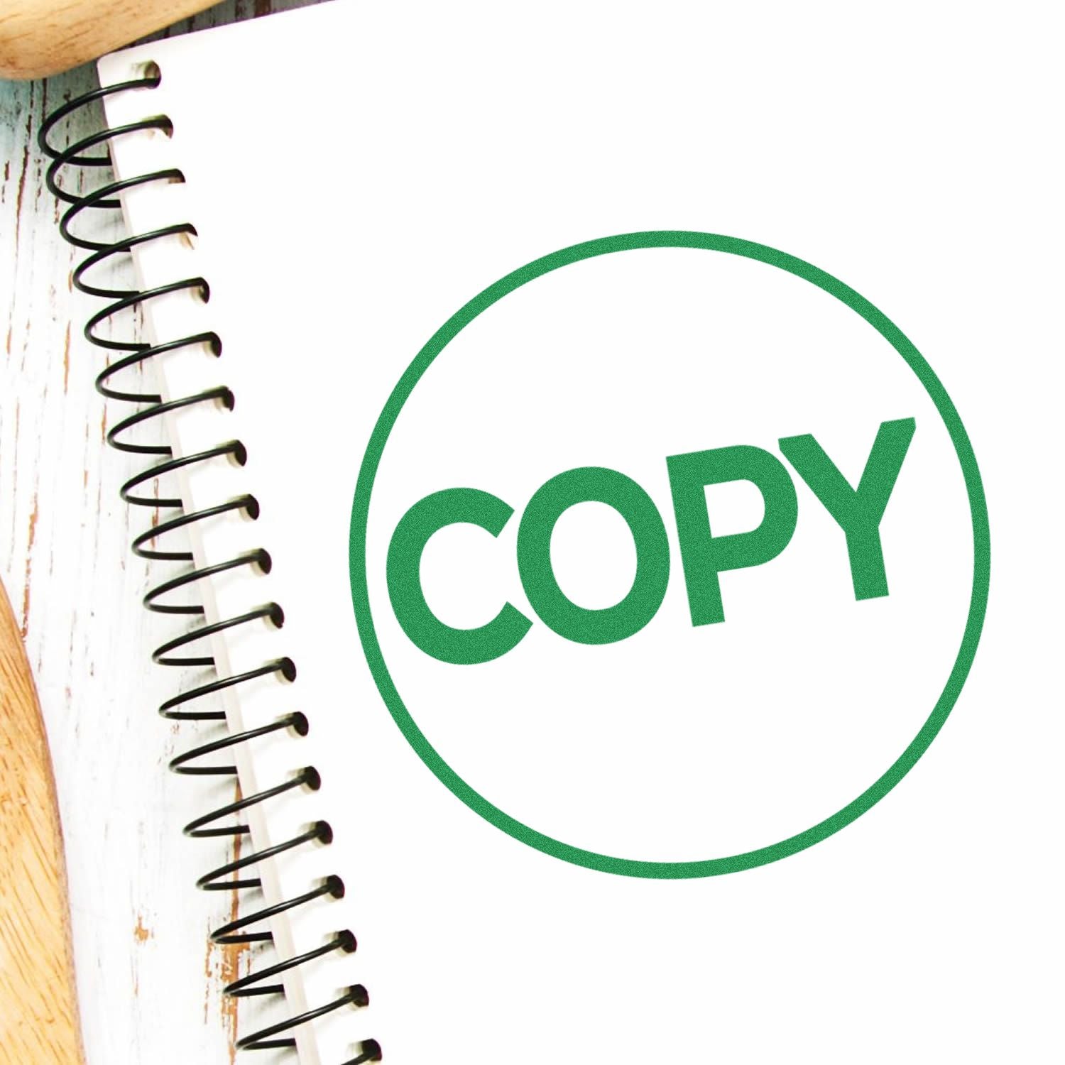 Round Copy Rubber Stamp in green ink on a white spiral notebook, placed on a wooden surface.