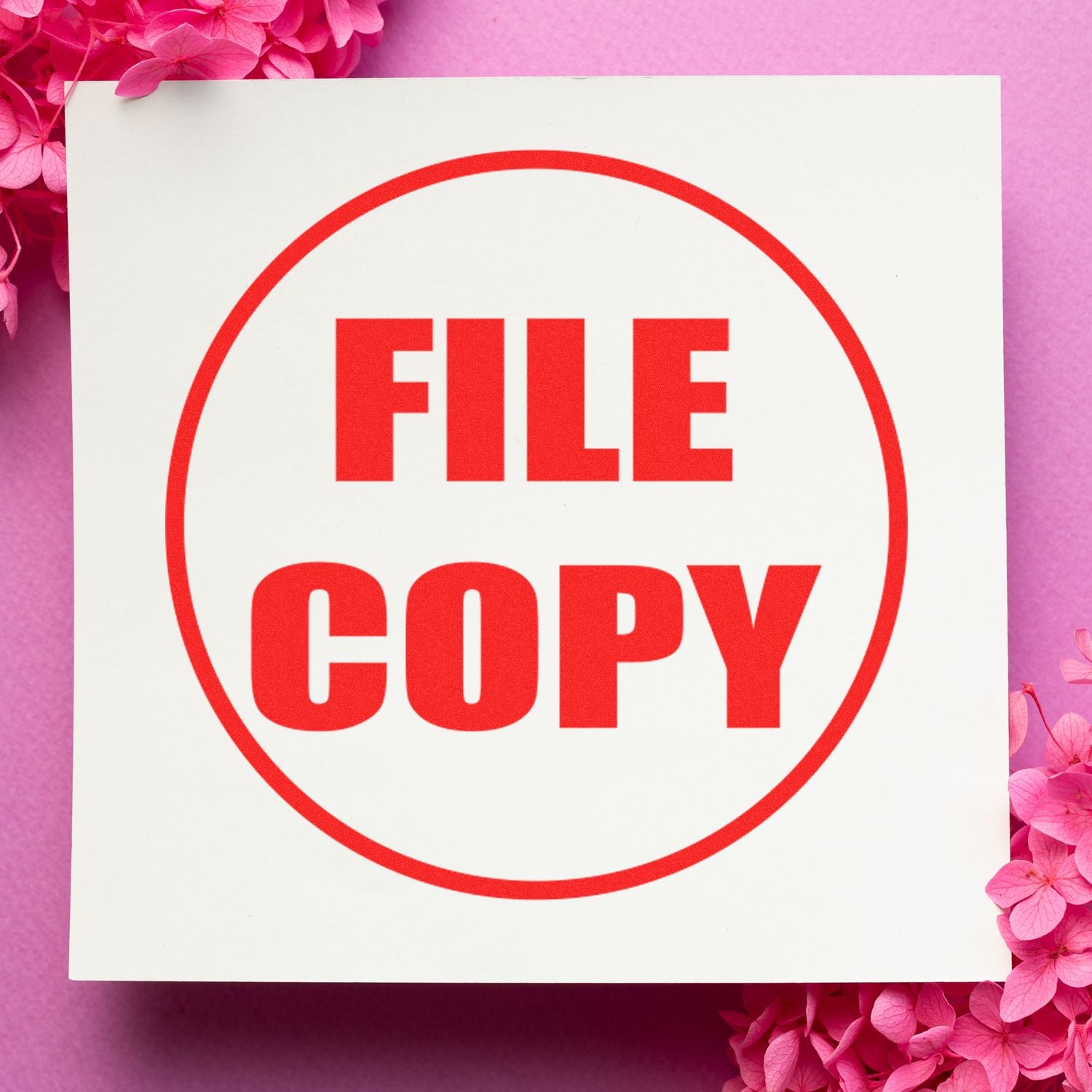 Round Draft Rubber Stamp with FILE COPY in bold red letters on white paper, surrounded by pink flowers on a pink background.