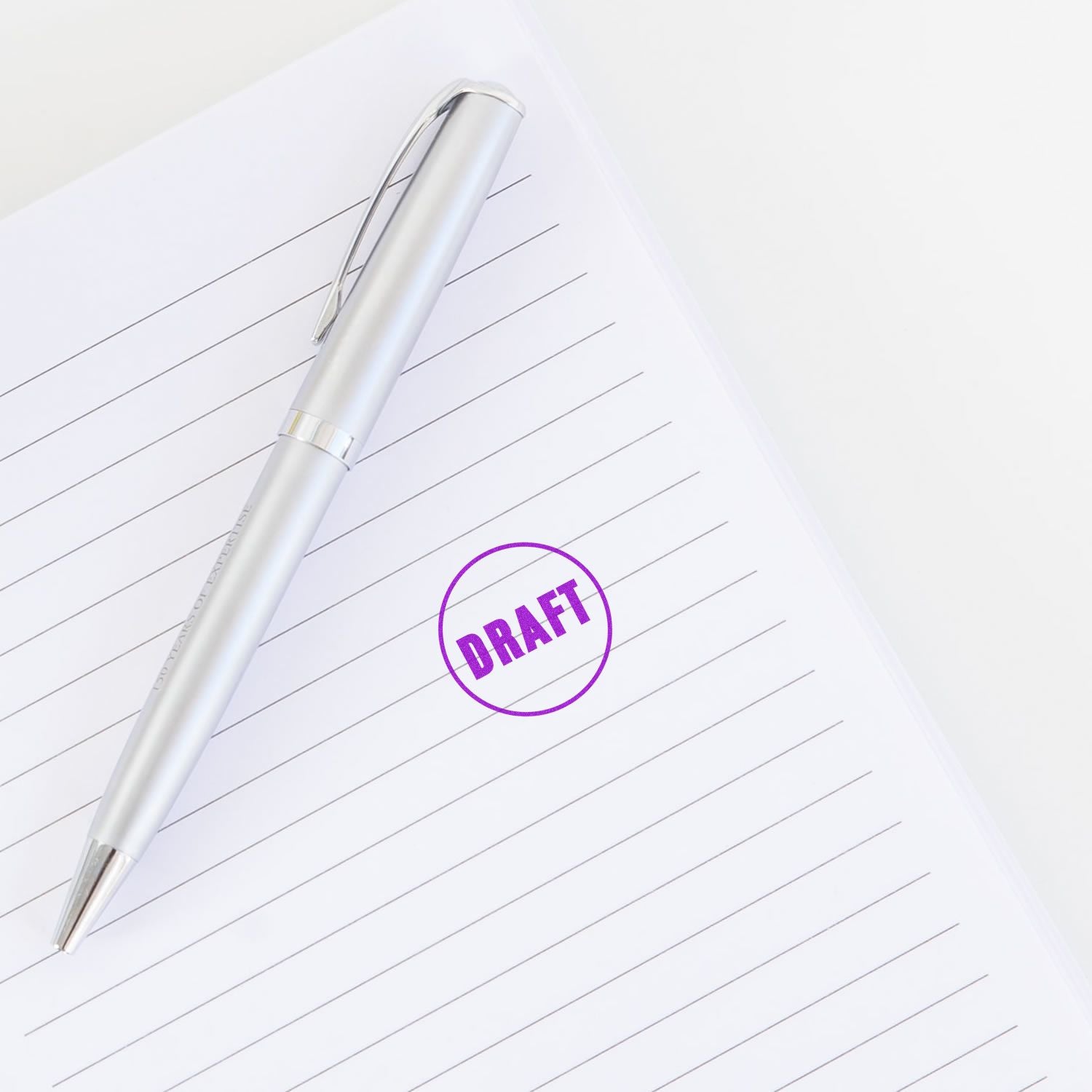 Silver pen on lined paper with a purple round draft rubber stamp marking the word 'DRAFT' in the center.