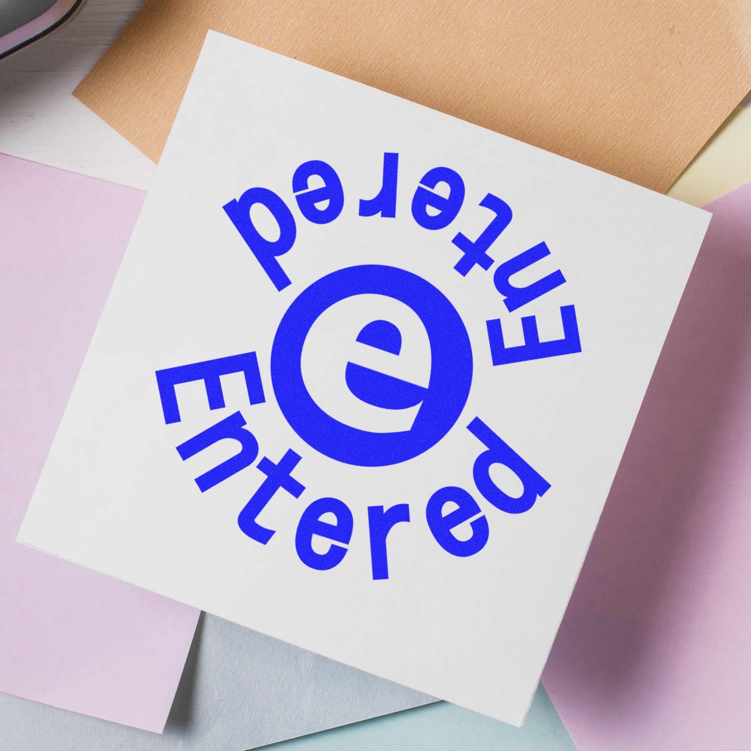 Round Entered Entered rubber stamp with blue text on white paper, surrounded by pastel-colored papers.