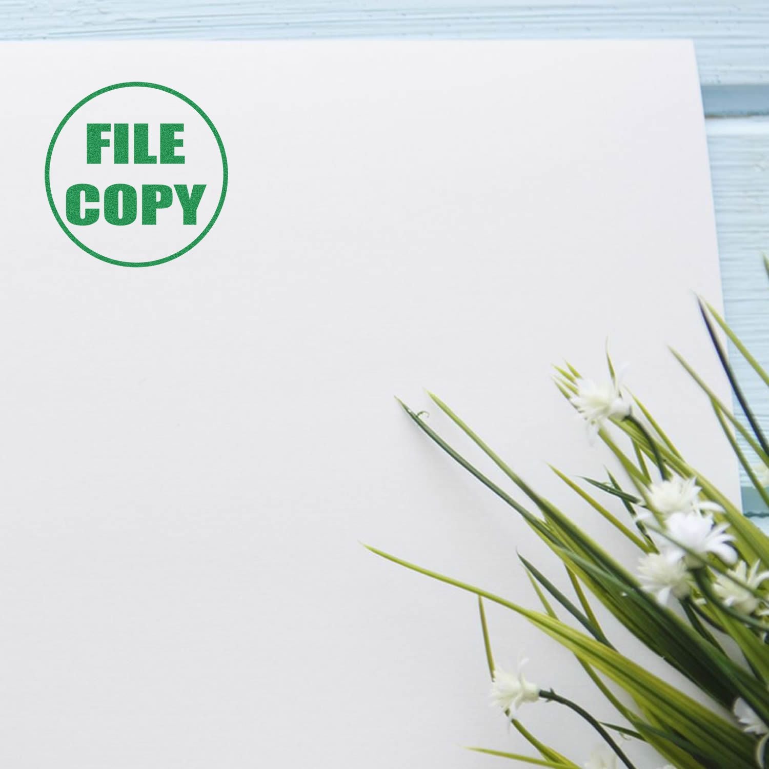 Round File Copy rubber stamp in green ink on a white paper next to a small bouquet of white flowers and green leaves.