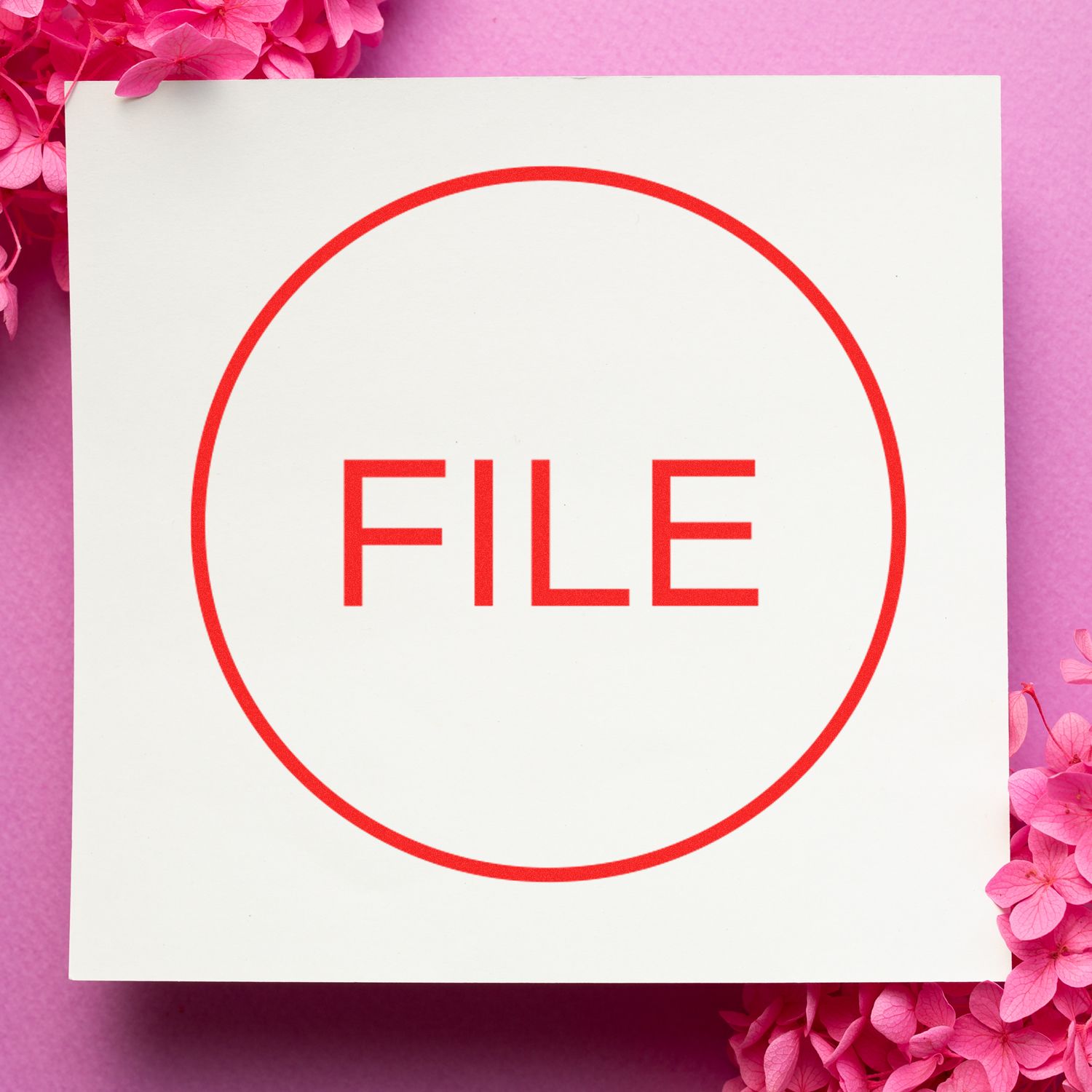 Round File Rubber Stamp with the word FILE in red inside a circle on white paper, surrounded by pink flowers on a pink background.