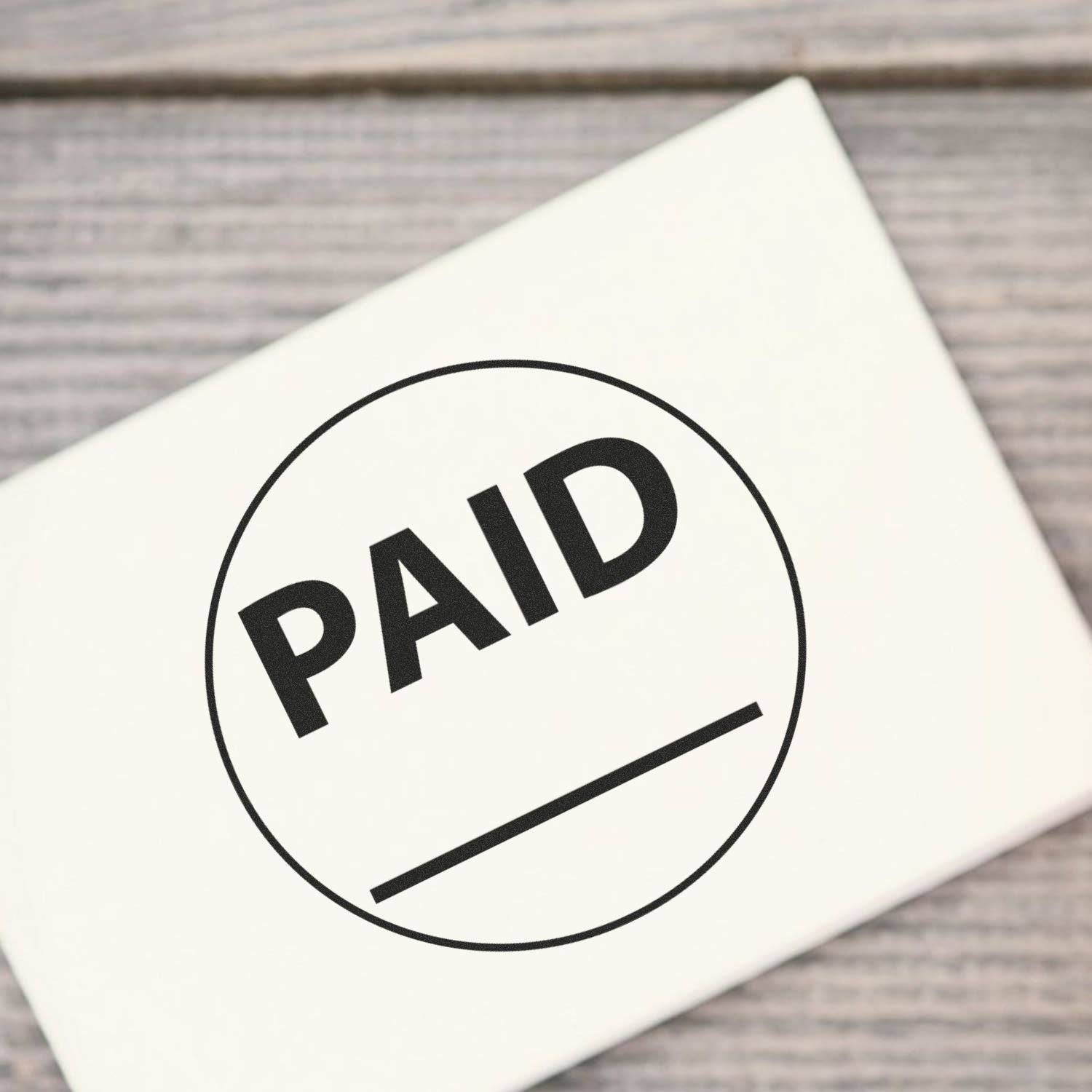 Round Paid with Line Rubber Stamp marking "PAID" on a white surface, placed on a wooden background.