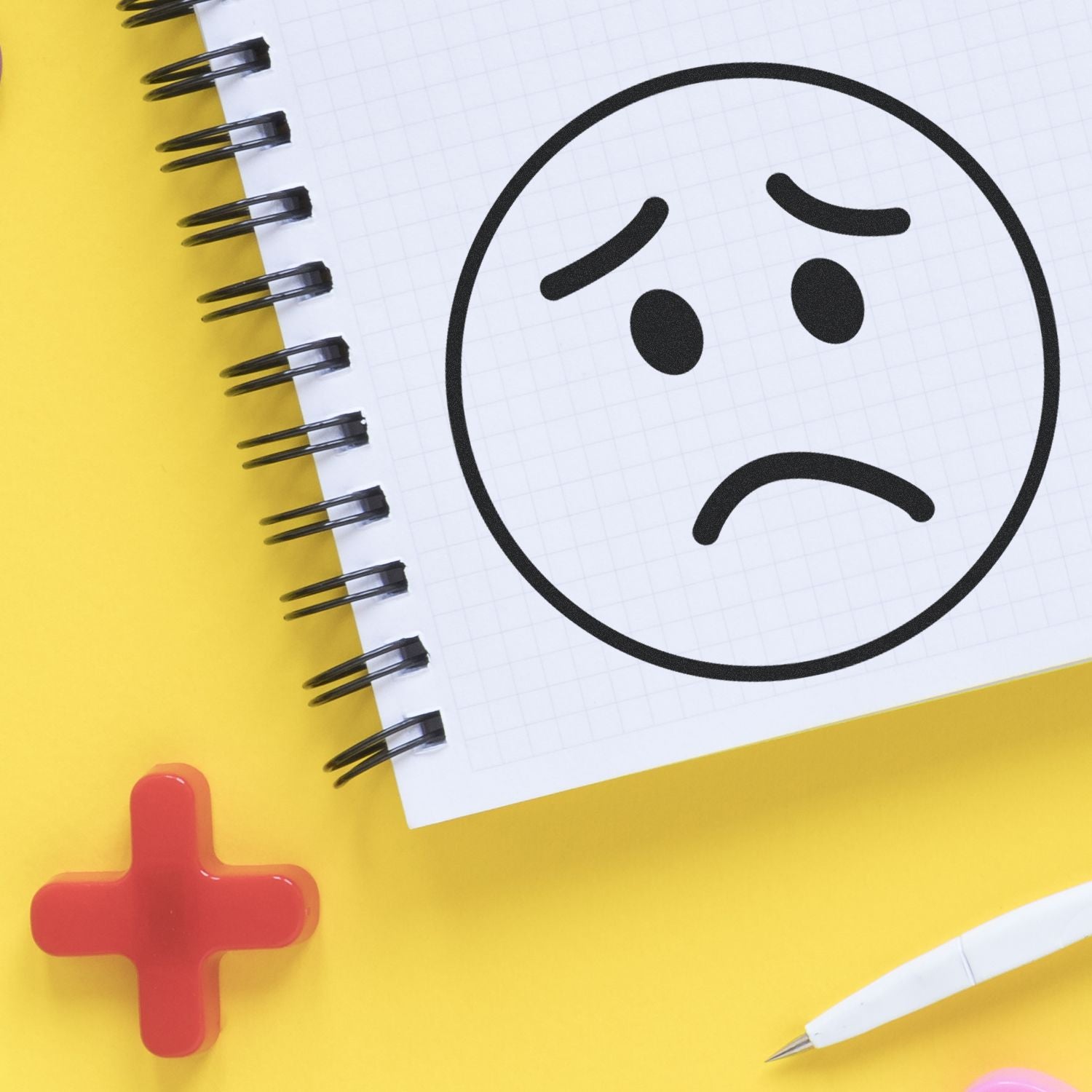 Round Sad Face Rubber Stamp on a spiral notebook with a red cross, white pen, and yellow background.