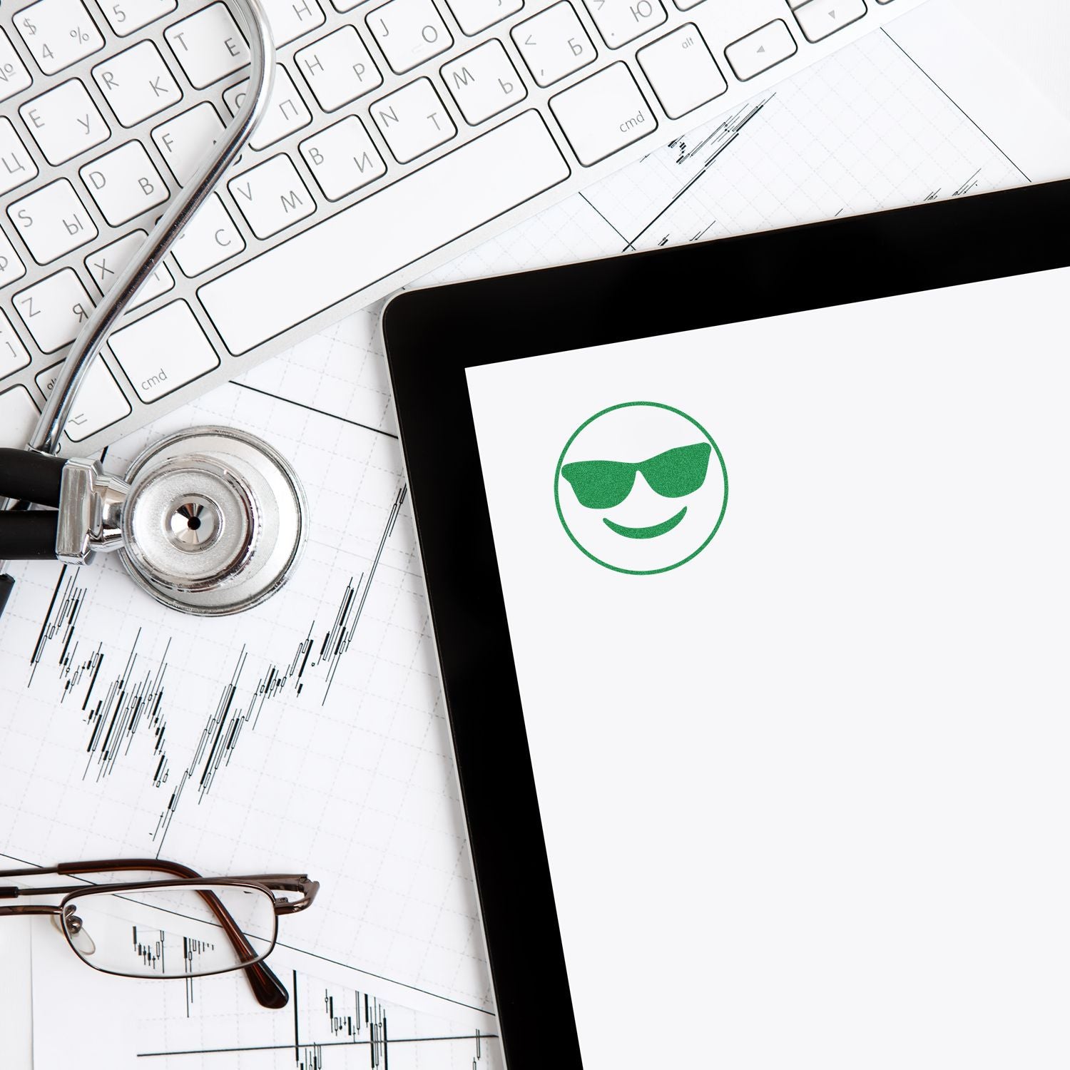 Round Smiley with Sunglasses Rubber Stamp on paper beside a stethoscope, glasses, keyboard, and tablet on a desk.