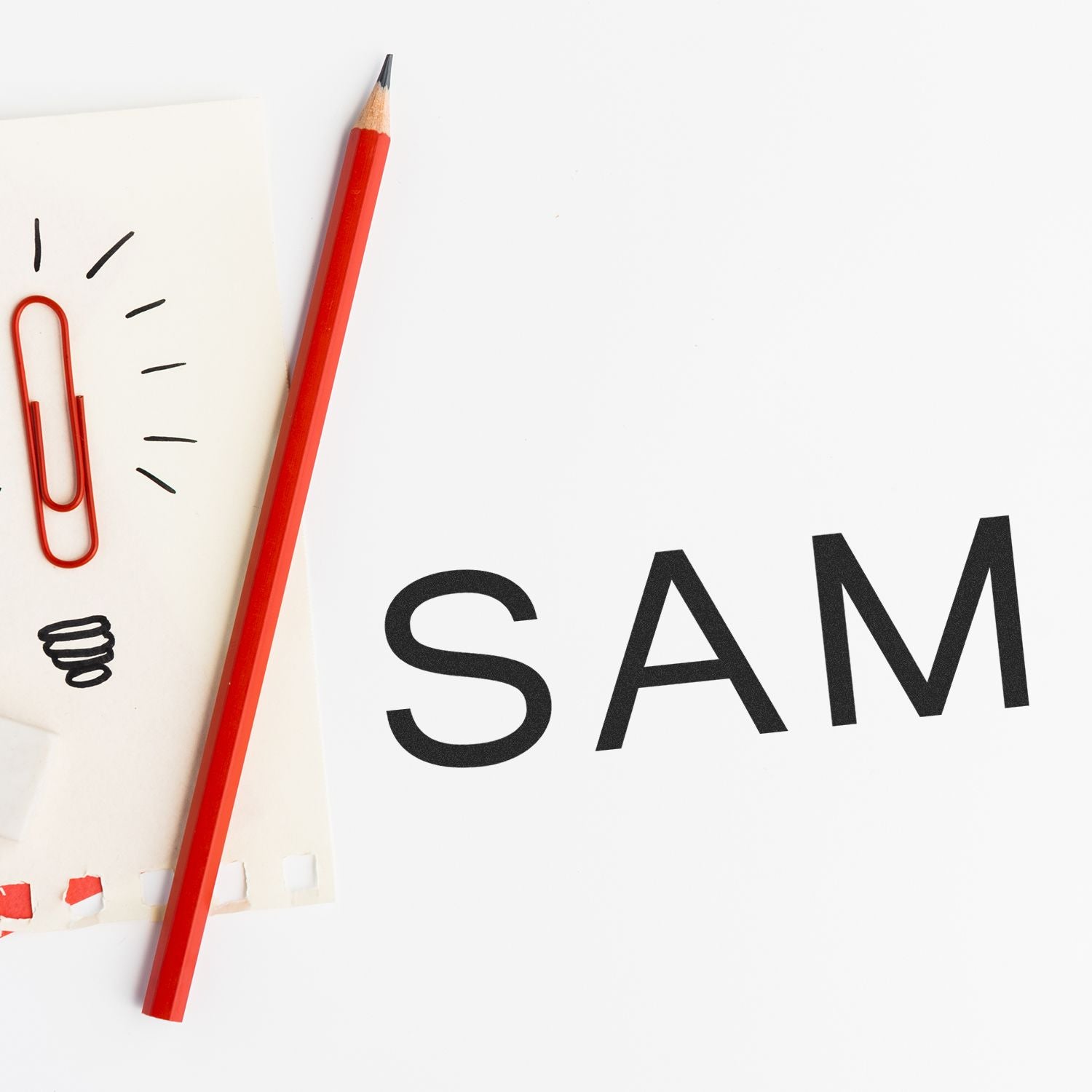 Slim Pre-Inked SAM Stamp imprint on white paper, next to a red pencil, paperclip, and a small notepad with doodles.