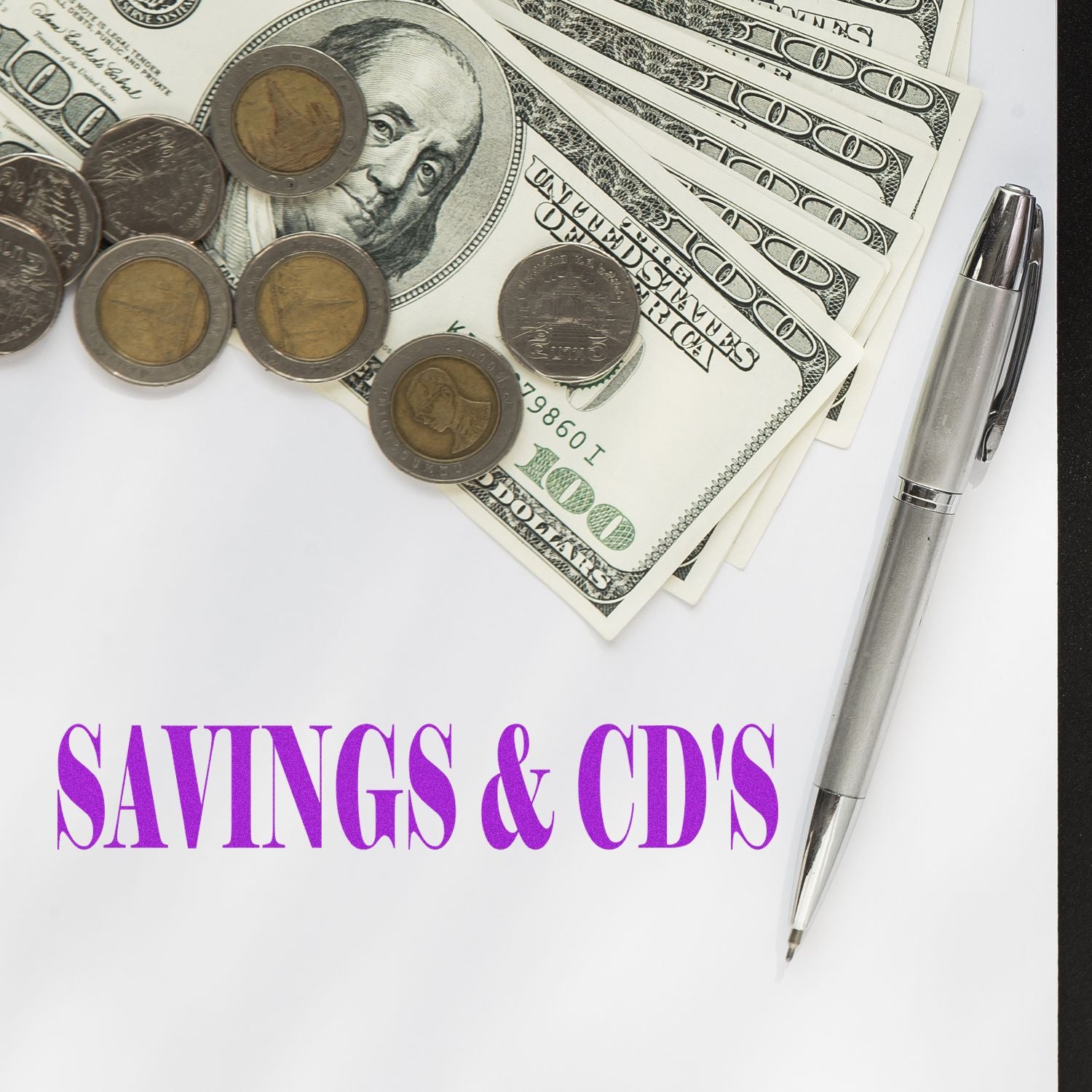 Savings & CDs rubber stamp with US dollar bills, coins, and a silver pen on a white background.