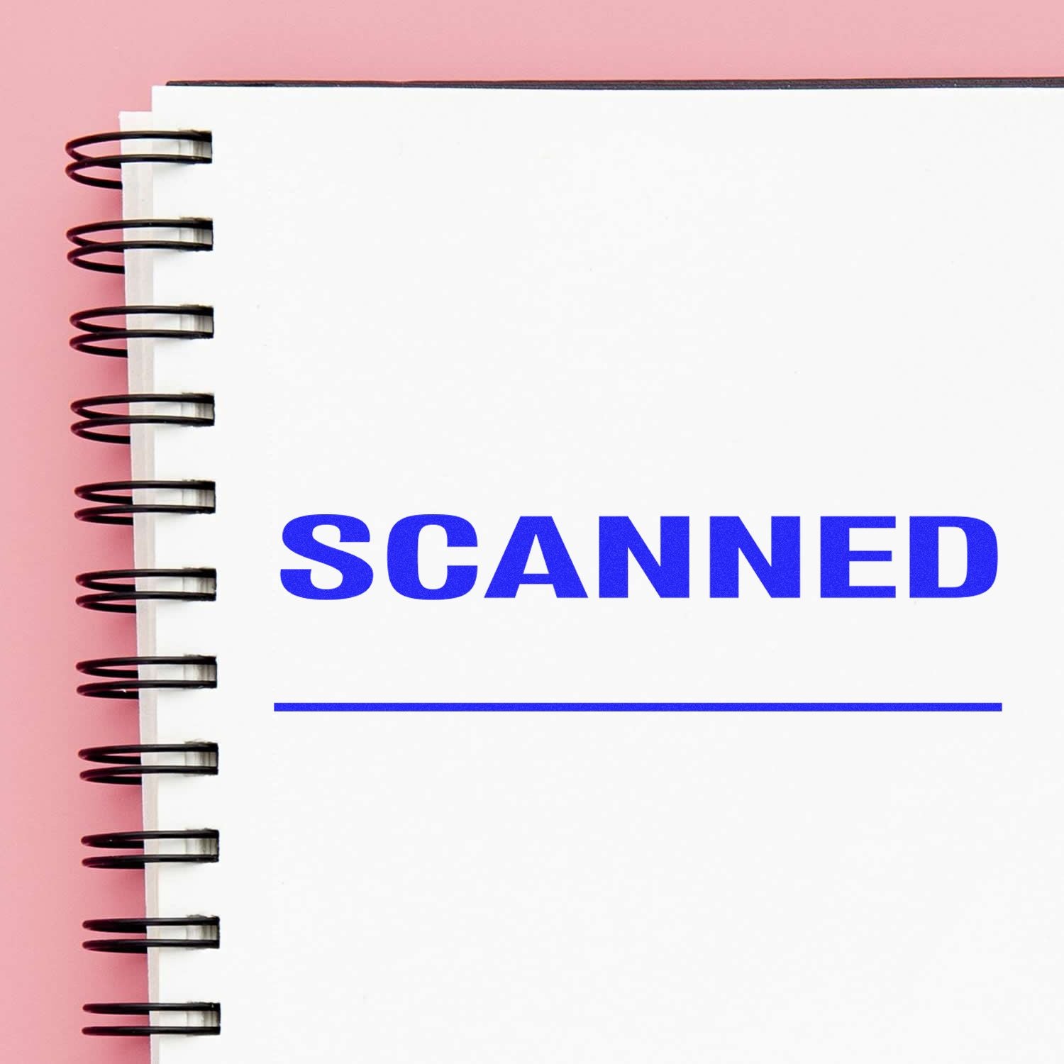 A notebook with a spiral binding on a pink background, featuring a blue Scanned with Line Rubber Stamp and a blank line underneath.