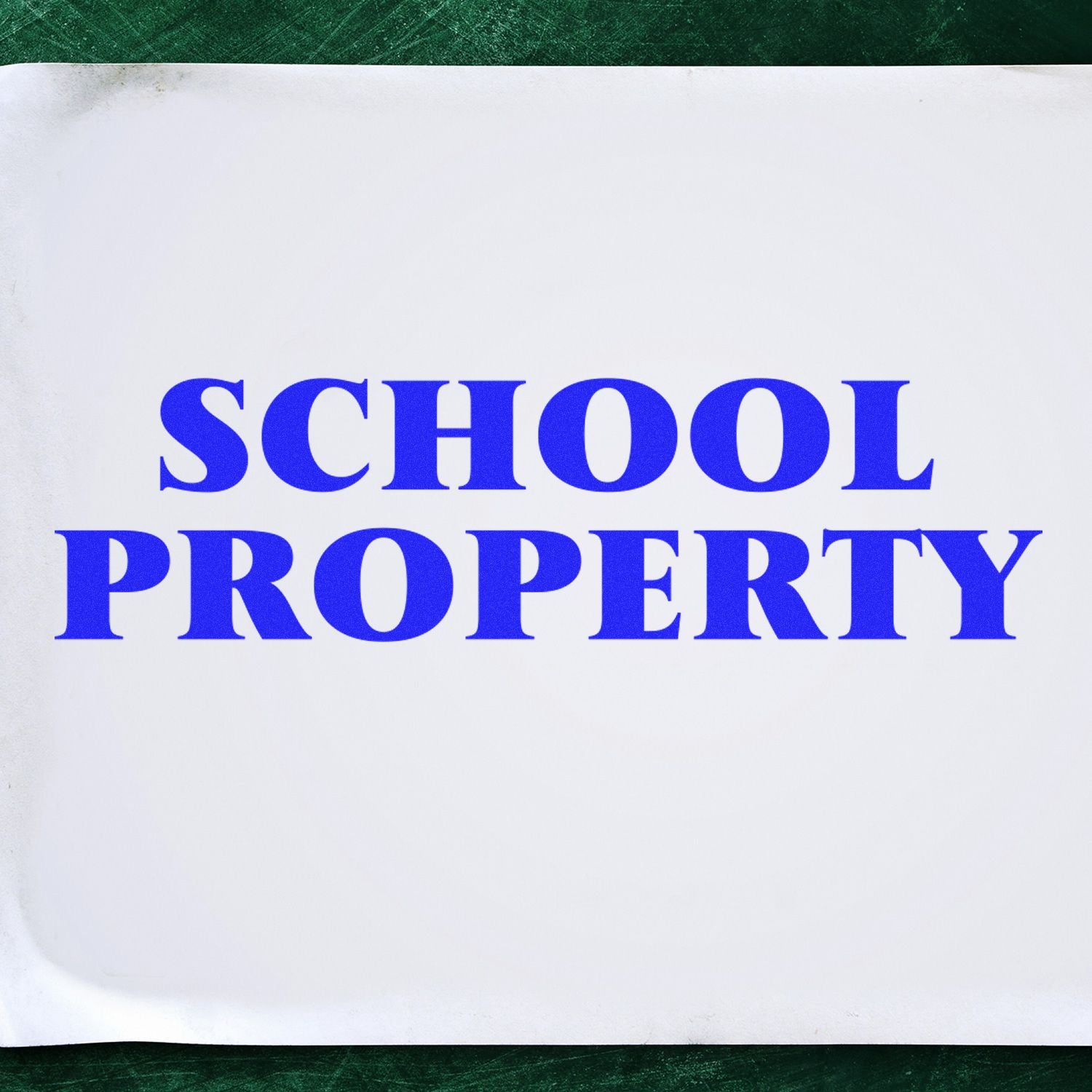 Blue 'School Property' rubber stamp impression on white paper, placed on a green surface.