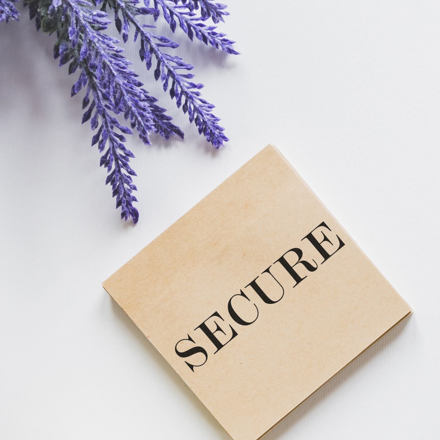 Secure rubber stamp on a beige square block, placed on a white surface next to sprigs of purple lavender flowers.