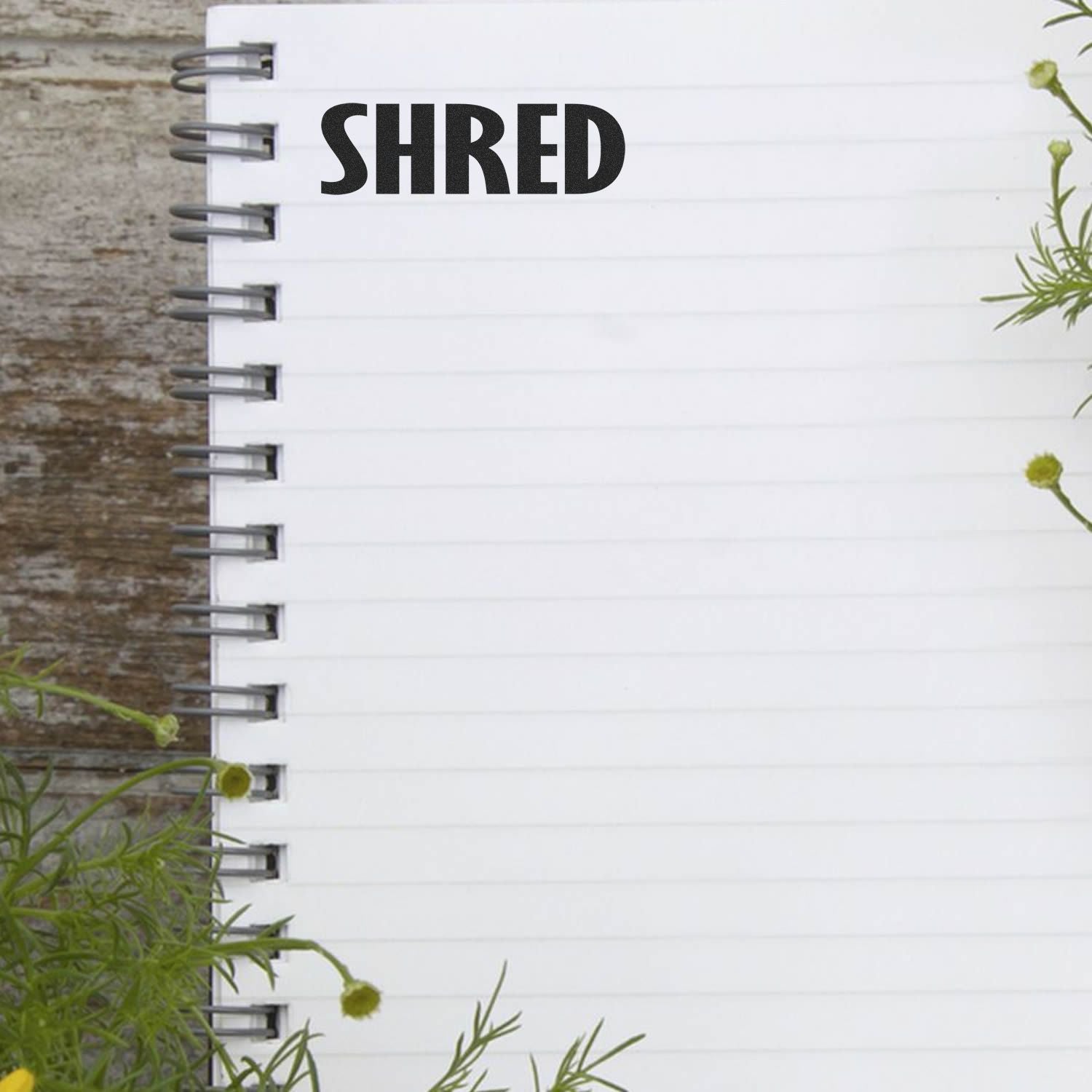 Shred Rubber Stamp impression on a blank spiral notebook page with green plants in the background.