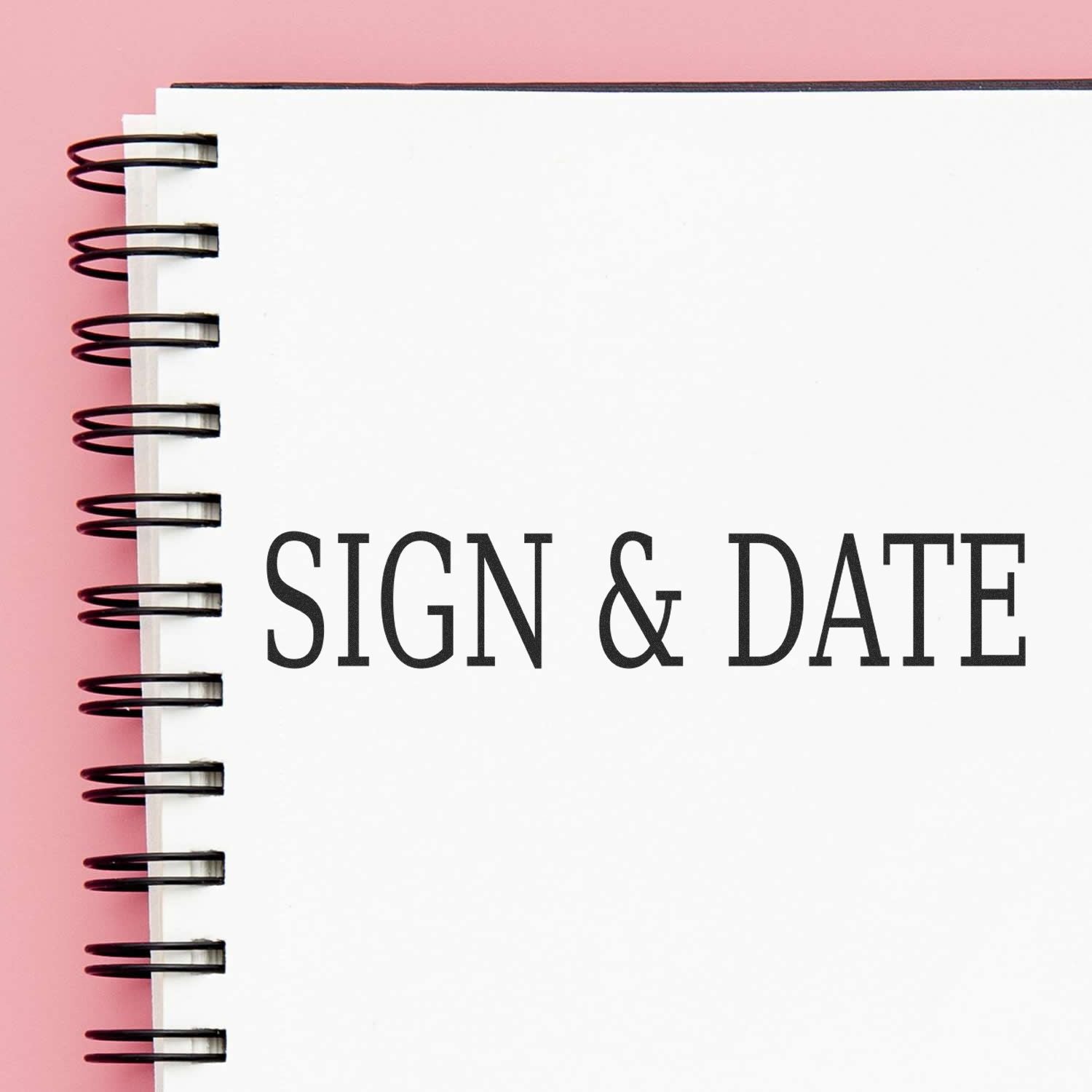 Slim Pre-Inked Sign & Date Stamp used on a white spiral notebook with SIGN & DATE text, against a pink background.