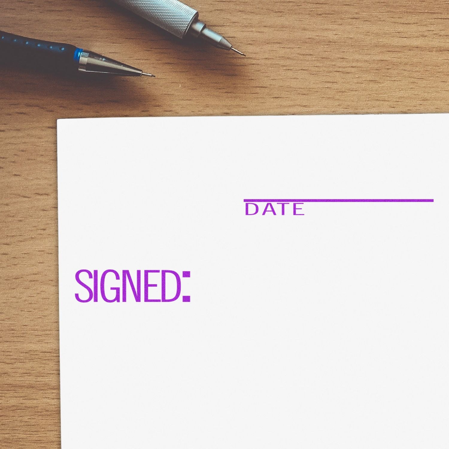 Signed with Date Rubber Stamp on white paper with spaces for signature and date, placed on a wooden desk with pens.