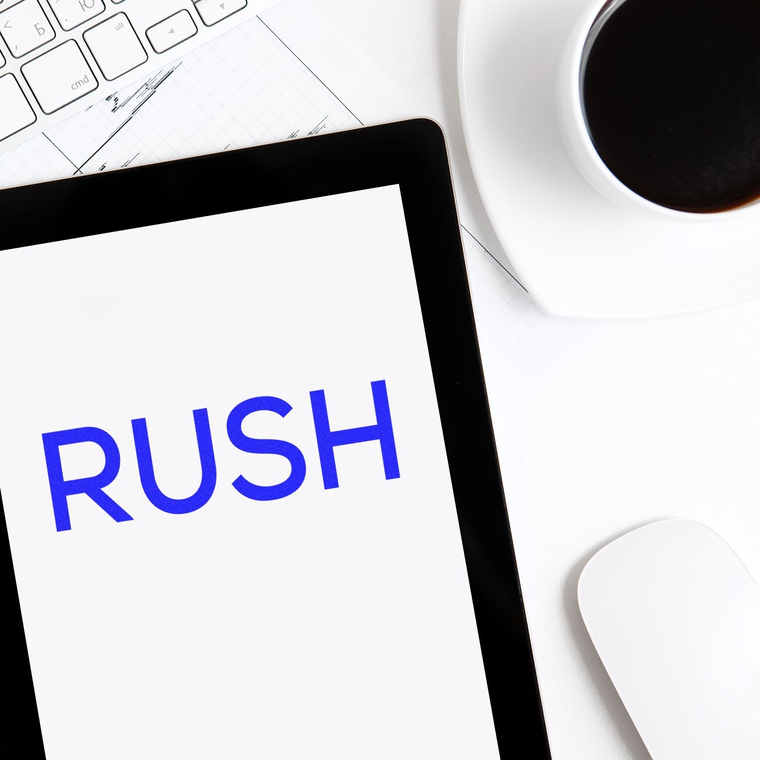 Self Inking Skinny Rush Stamp in use, stamping RUSH on paper near a keyboard, tablet, and coffee cup on a white desk.