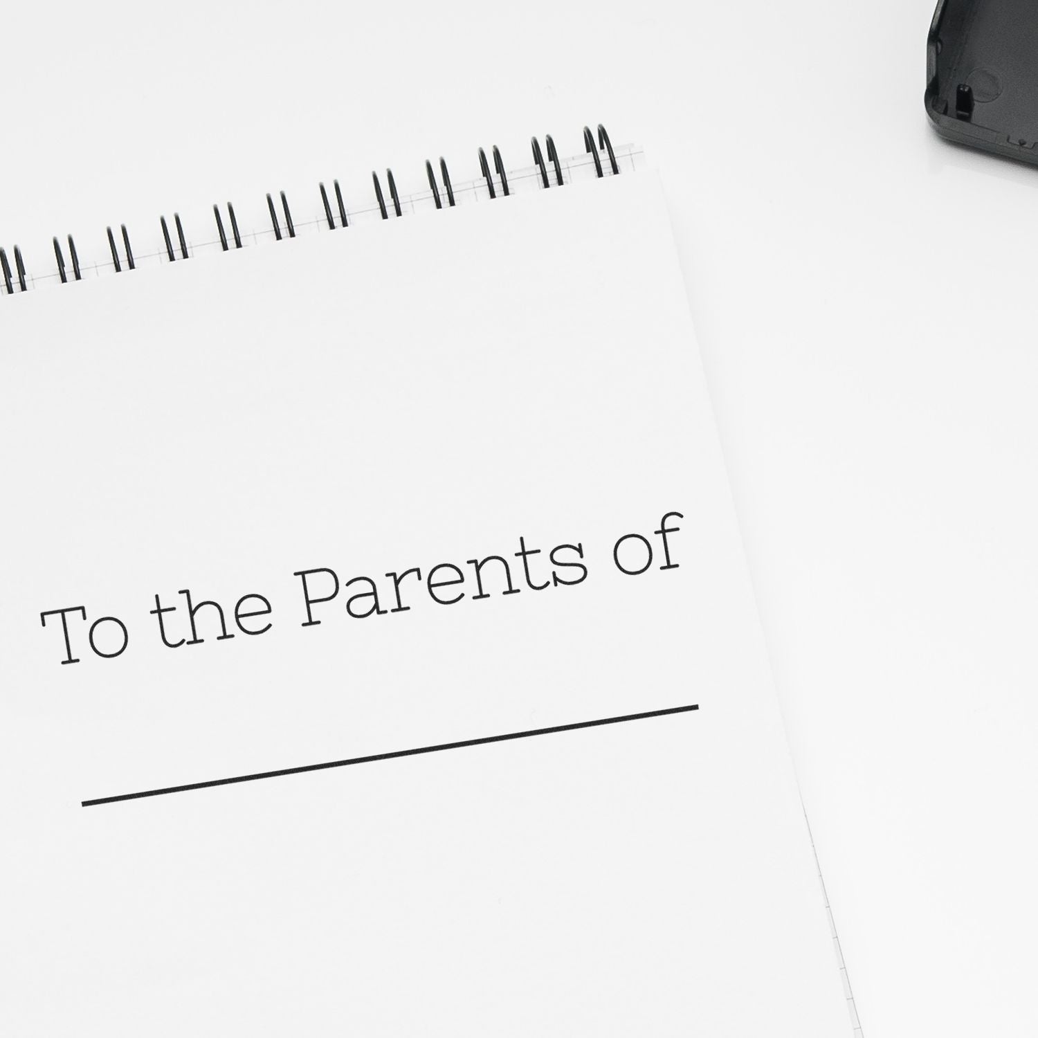 Skinny To the Parents of Rubber Stamp used on a white spiral notebook with text To the Parents of and a blank line below.