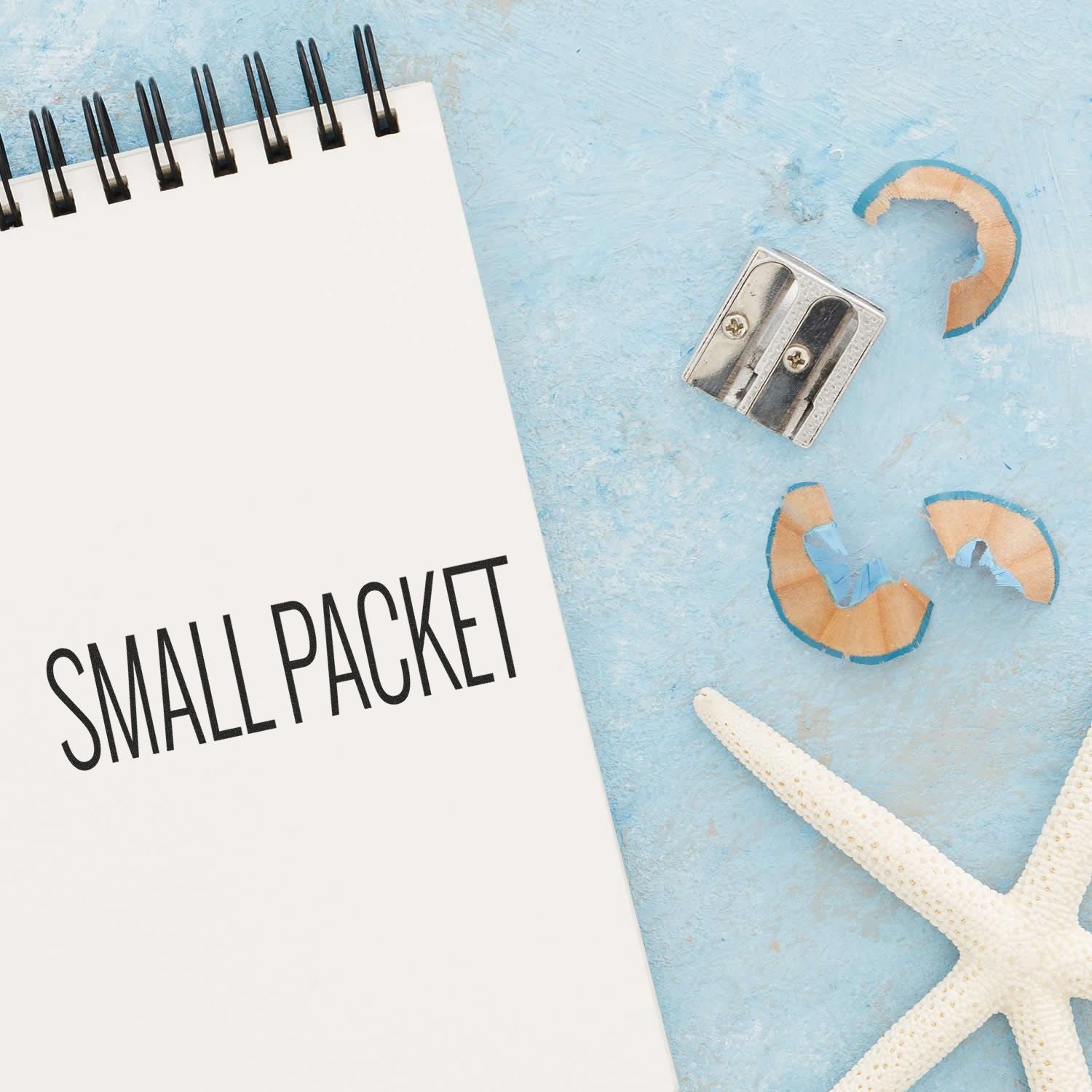 A Slim Pre-Inked Small Packet Stamp imprint on a notebook page, surrounded by a pencil sharpener, shavings, and a starfish.