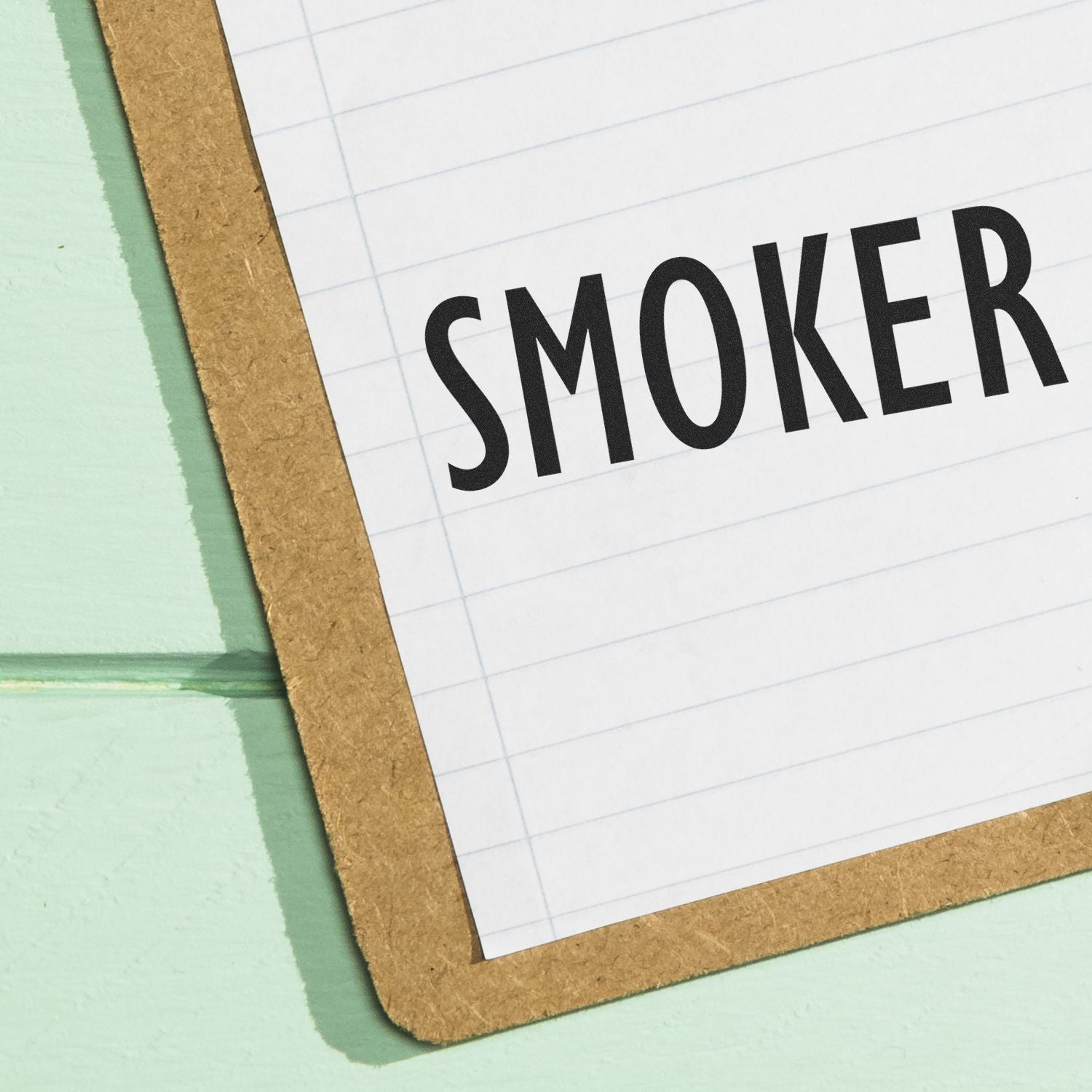 Paper stamped with 'SMOKER' using a Slim Pre-Inked Smoker Stamp on a clipboard with a light green background.