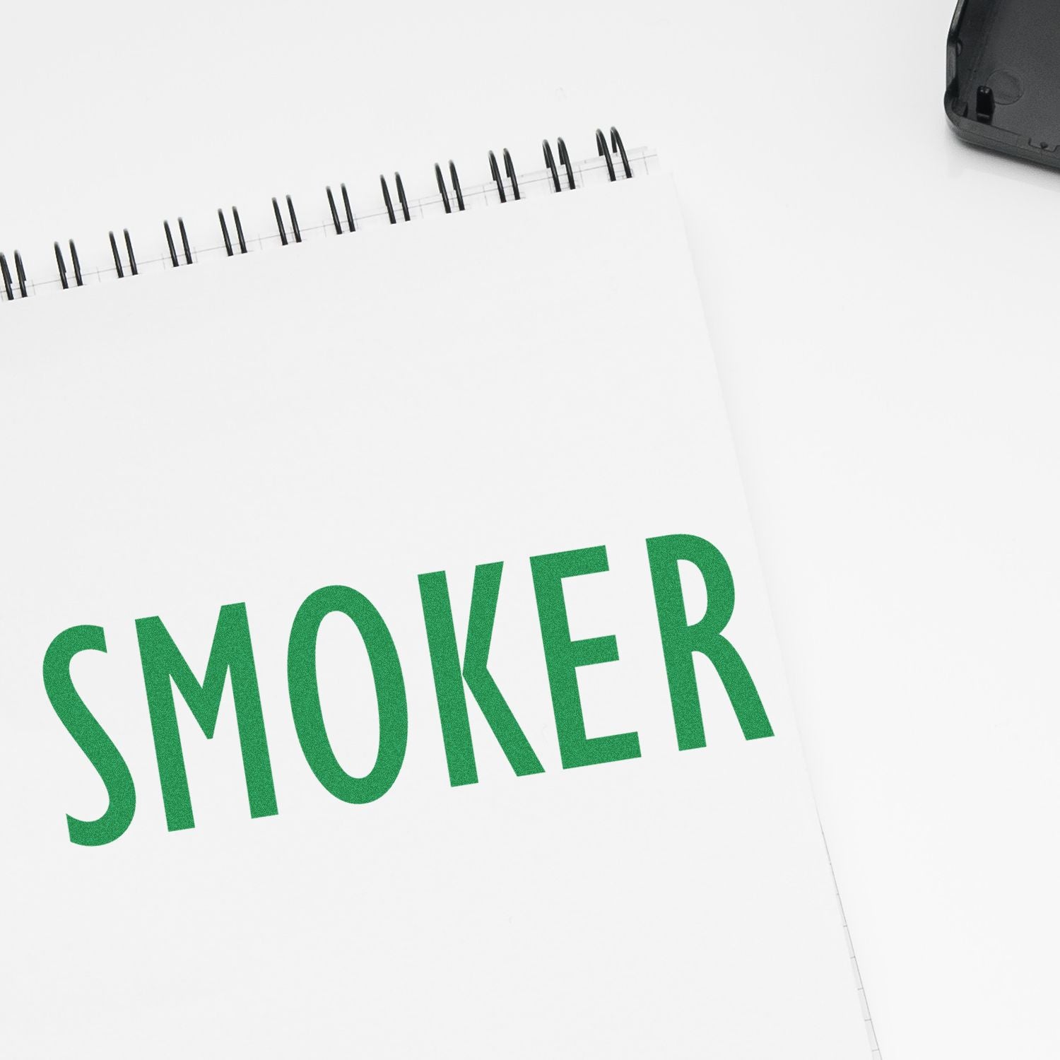 Slim Pre-Inked Smoker Stamp imprinting the word SMOKER in green ink on a white spiral-bound notebook.