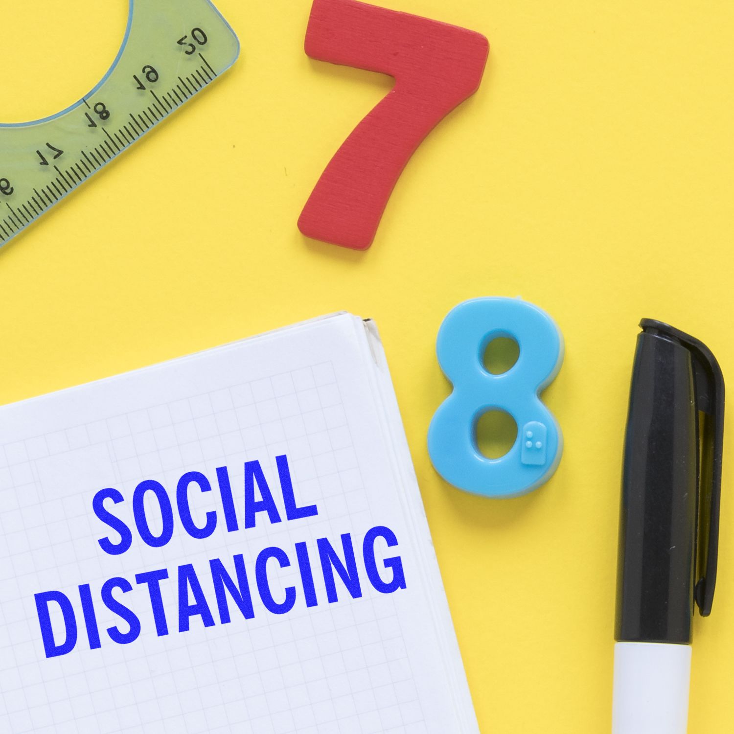 Social Distancing Rubber Stamp on a notebook with a pen, ruler, and colorful numbers on a yellow background.