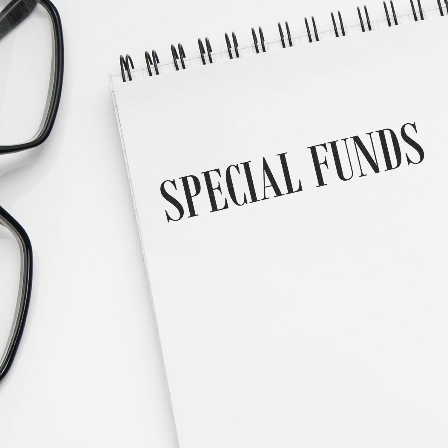 A notebook with "SPECIAL FUNDS" stamped on a page using the Special Funds Rubber Stamp, next to a pair of glasses.